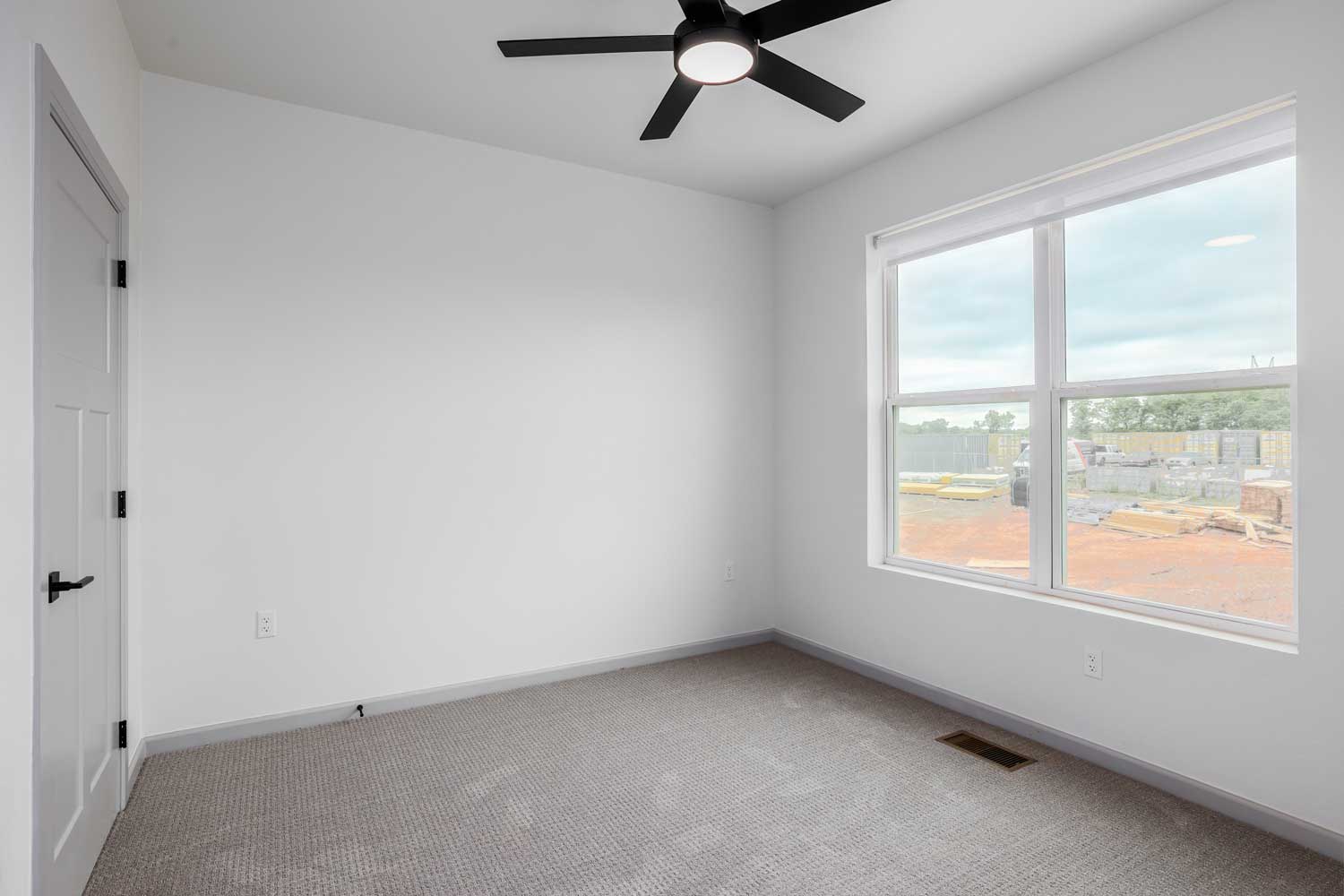 Spacious bedroom with carpet flooring, ceiling fan, large window, neutral painted walls, and recessed floor vent below inside