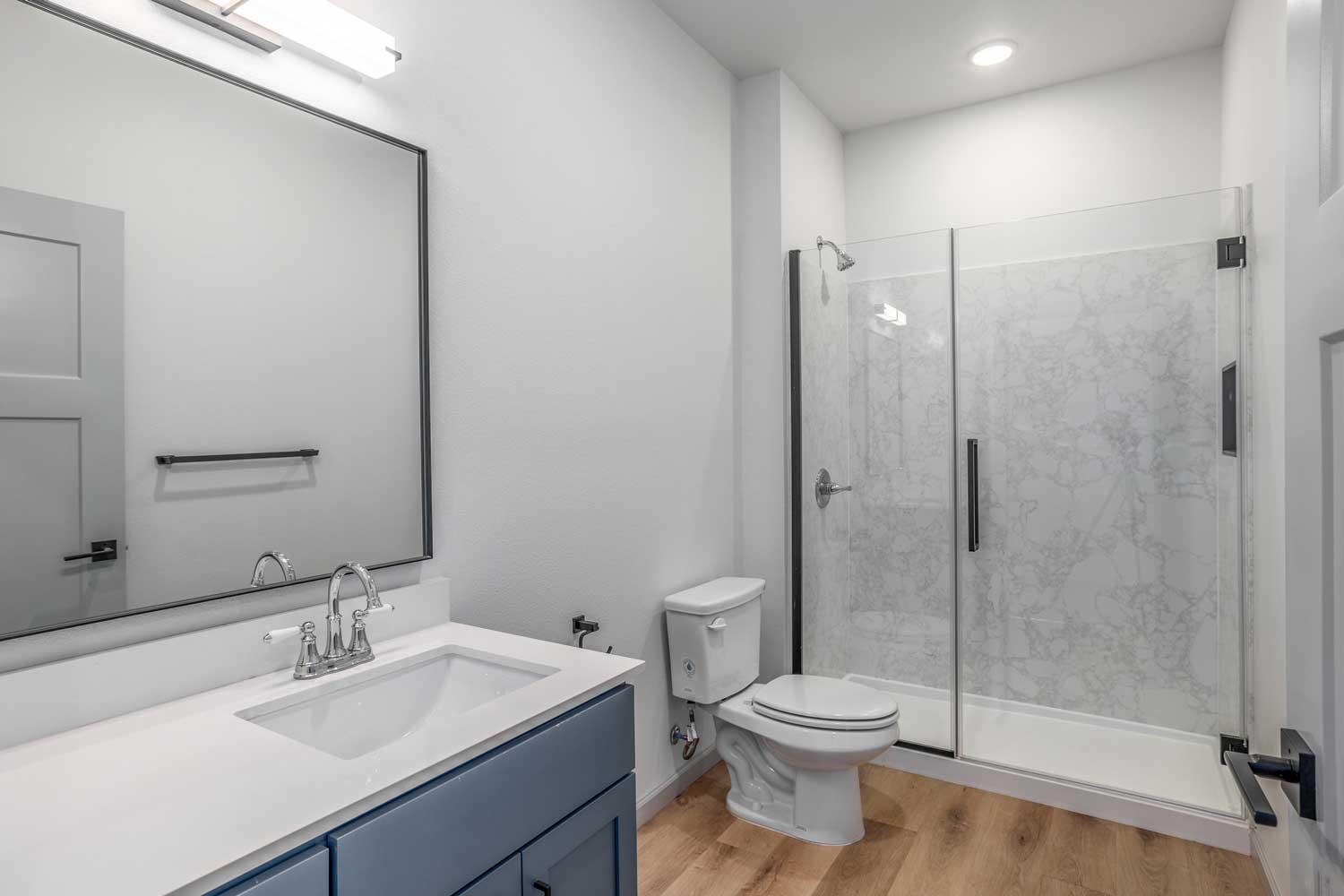 Modern bathroom with framed mirror, single vanity, glass walk-in shower, wood-style flooring, and marble-look wall panels