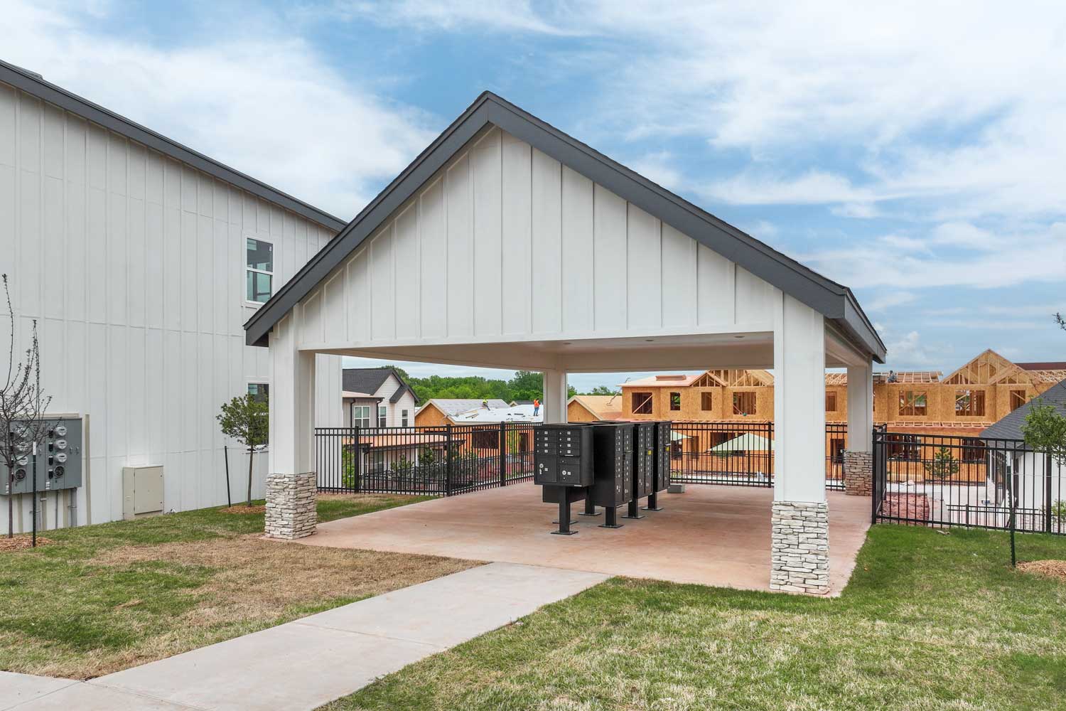 Covered community mailbox area with black parcel lockers, stone columns, and nearby apartment buildings and sidewalks nearby