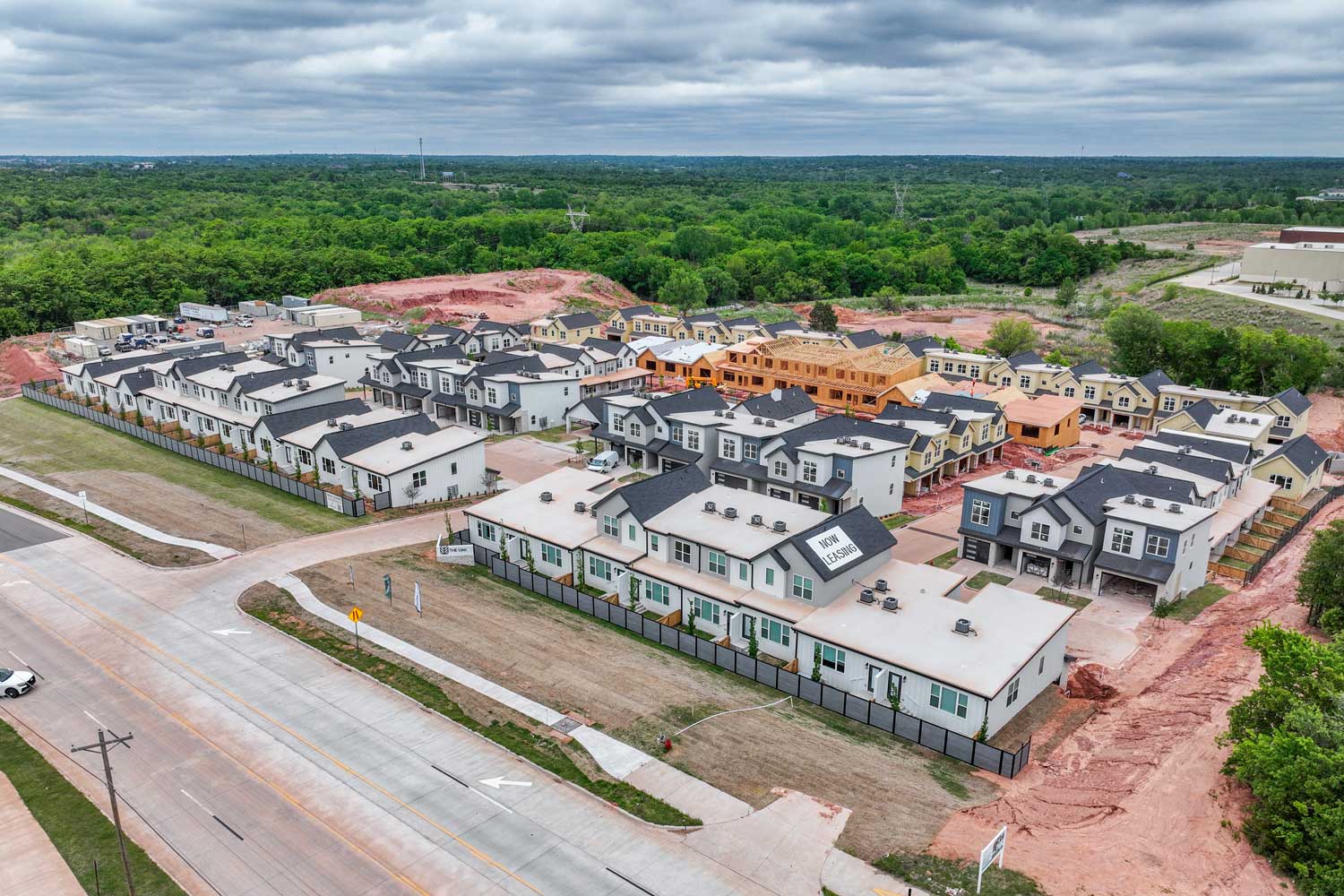 Elevated view of apartment homes with fenced yards, leasing office, and nearby townhomes under construction below today now