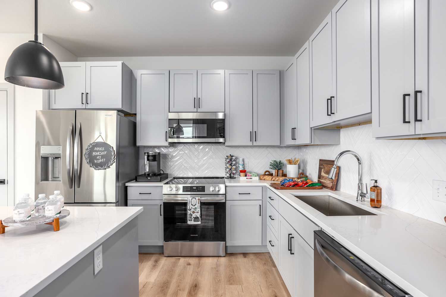 Contemporary kitchen with gray cabinetry, stainless steel appliances, white counters, and pendant lighting overhead