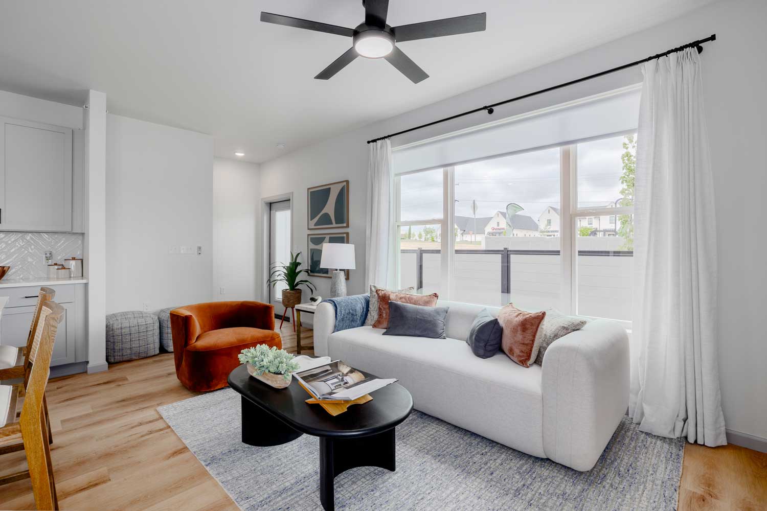 Open living room with large windows, ceiling fan, modern seating, wood-style flooring, and neutral wall finishes