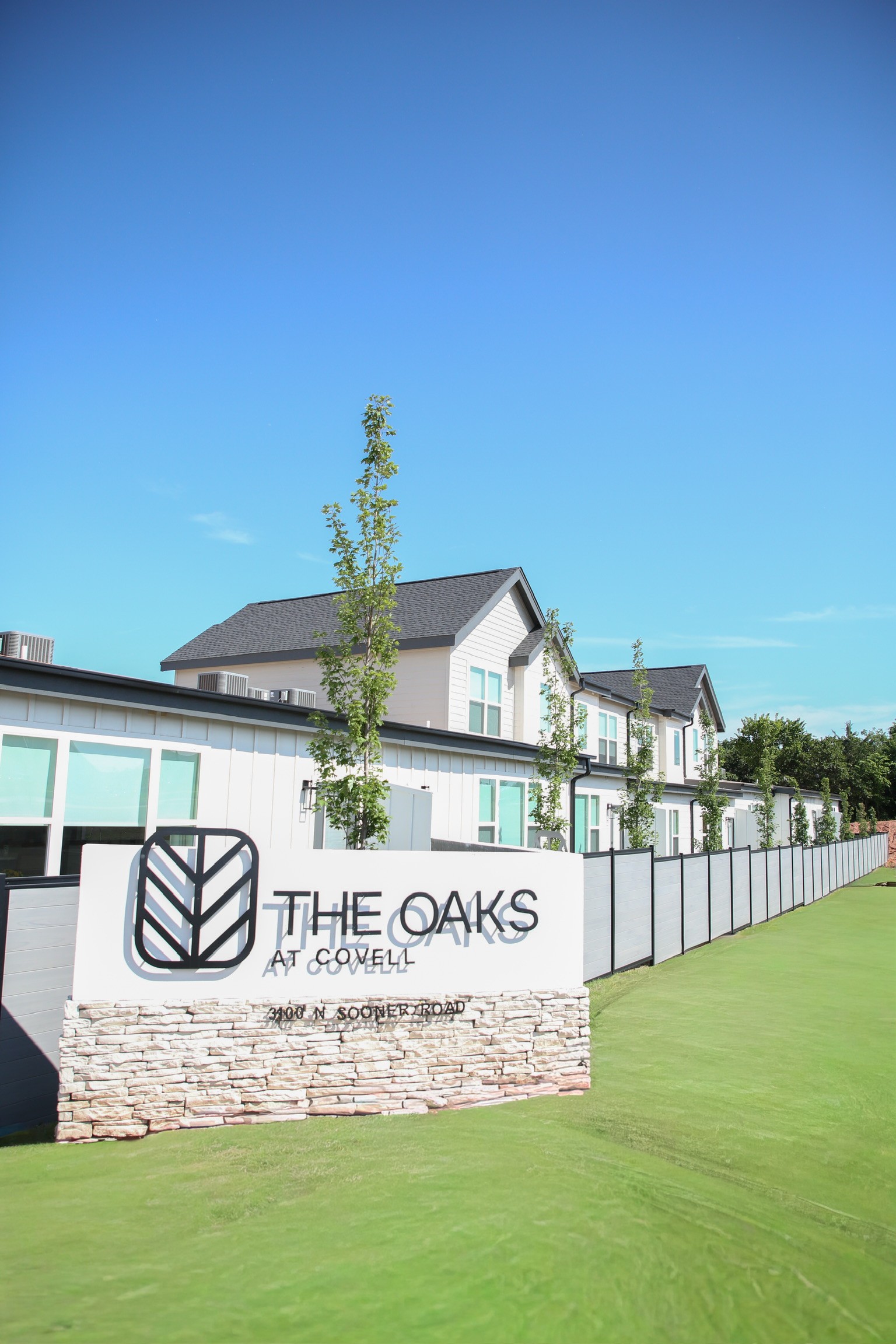 The Oaks at Covell welcome monument sign with stone base, black iron fencing, and community buildings behind