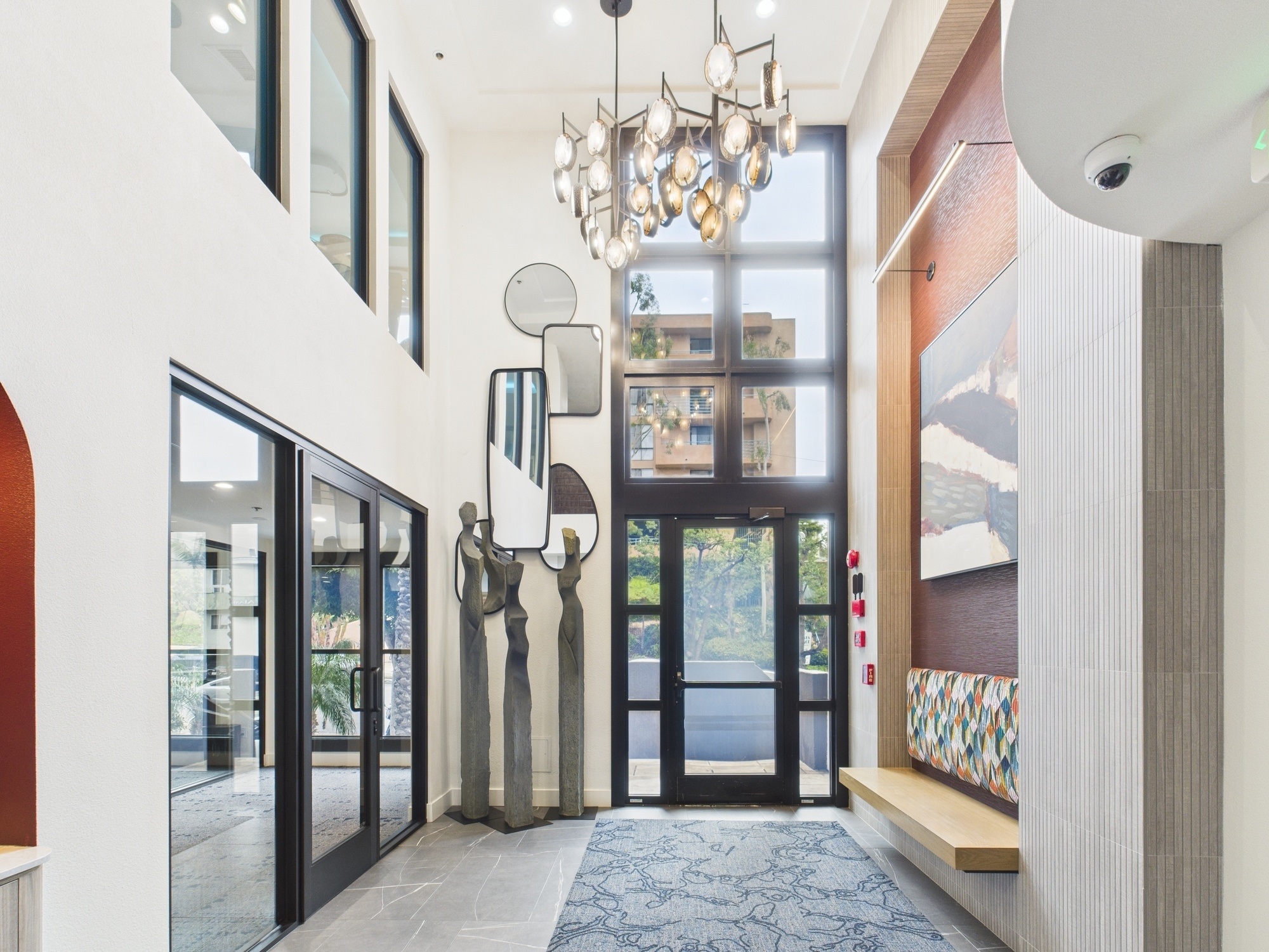 Modern apartment lobby with high ceilings, abstract art, curved balcony, patterned seating, and sleek contemporary décor