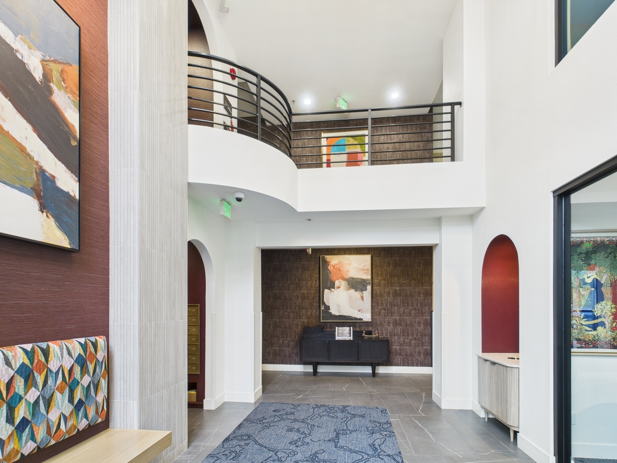 Bright lobby entrance with floor-to-ceiling windows, sculptures, mirrors, chandelier, and colorful bench seating