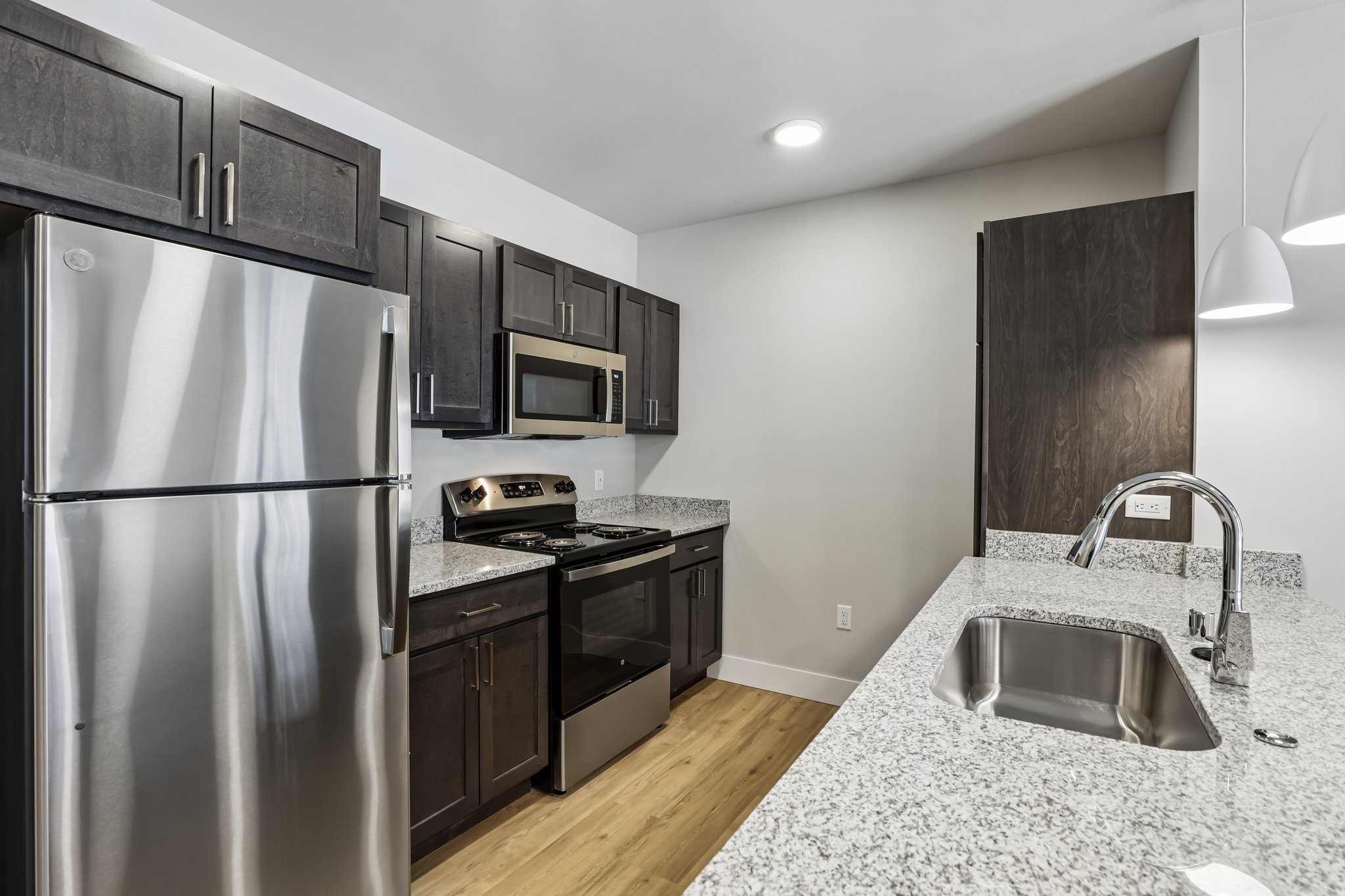 Kitchen in a one-bedroom apartment at The Victoria at Huxley Yards, an income-restricted 55+ senior apartment community in Madison, WI, featuring stainless steel appliances, granite countertops, and a kitchen island.
