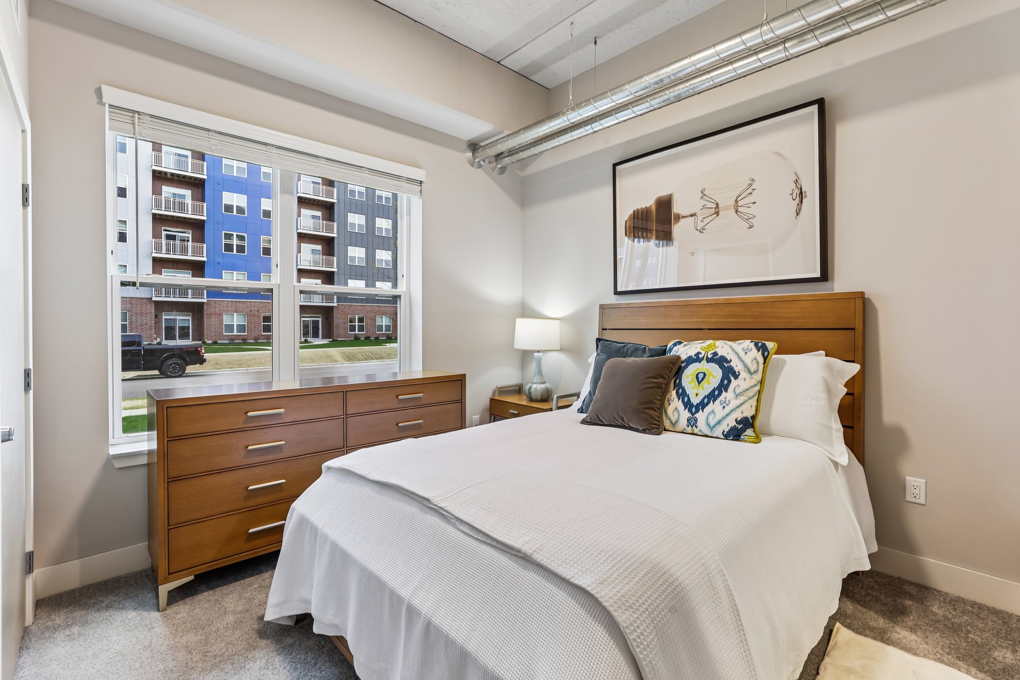 Bedroom in a one-bedroom senior apartment at The Victoria at Huxley Yards in Madison, WI, featuring carpeted floors, ceiling fan, and large window.