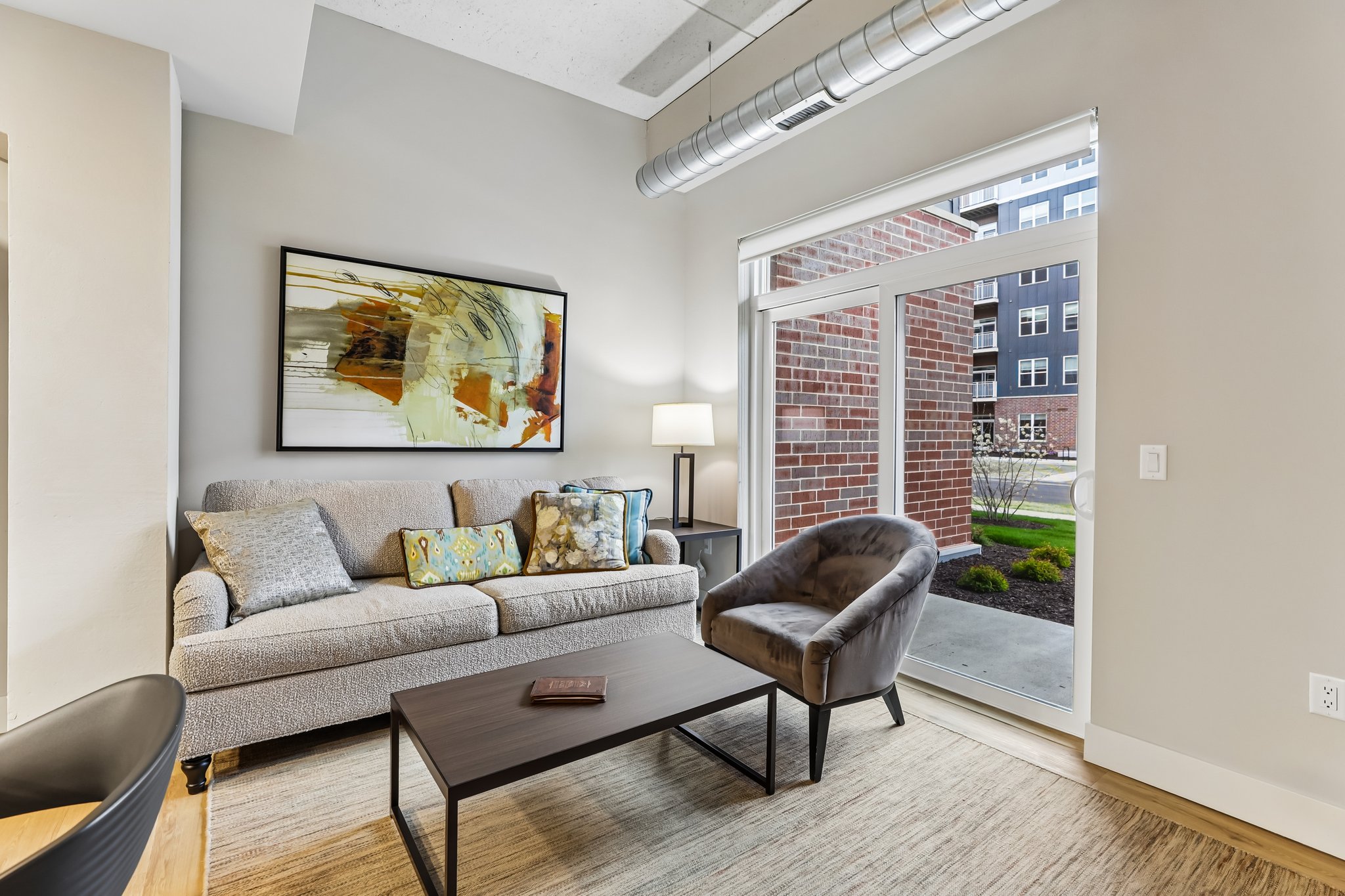 Living room in a one-bedroom income-restricted 55+ senior apartment at The Victoria at Huxley Yards in Madison, WI, with open layout, carpeted flooring, and natural light.