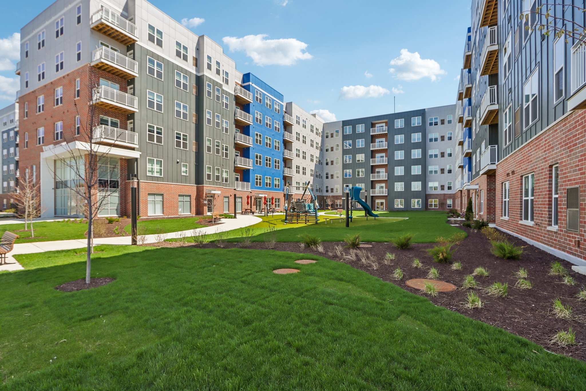 Landscaped courtyard surrounded by contemporary apartment buildings with a central pool, walking paths, seating areas, and green lawns