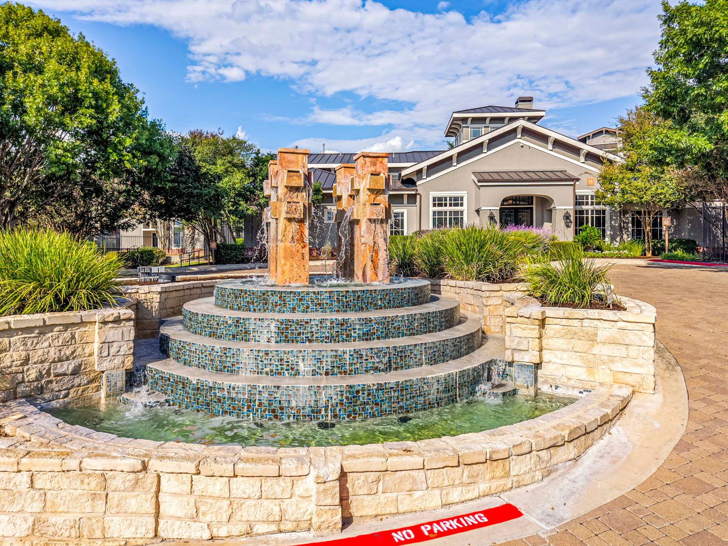Decorative stone water fountain with a mosaic tile basin at the community entrance, with the leasing office in the background