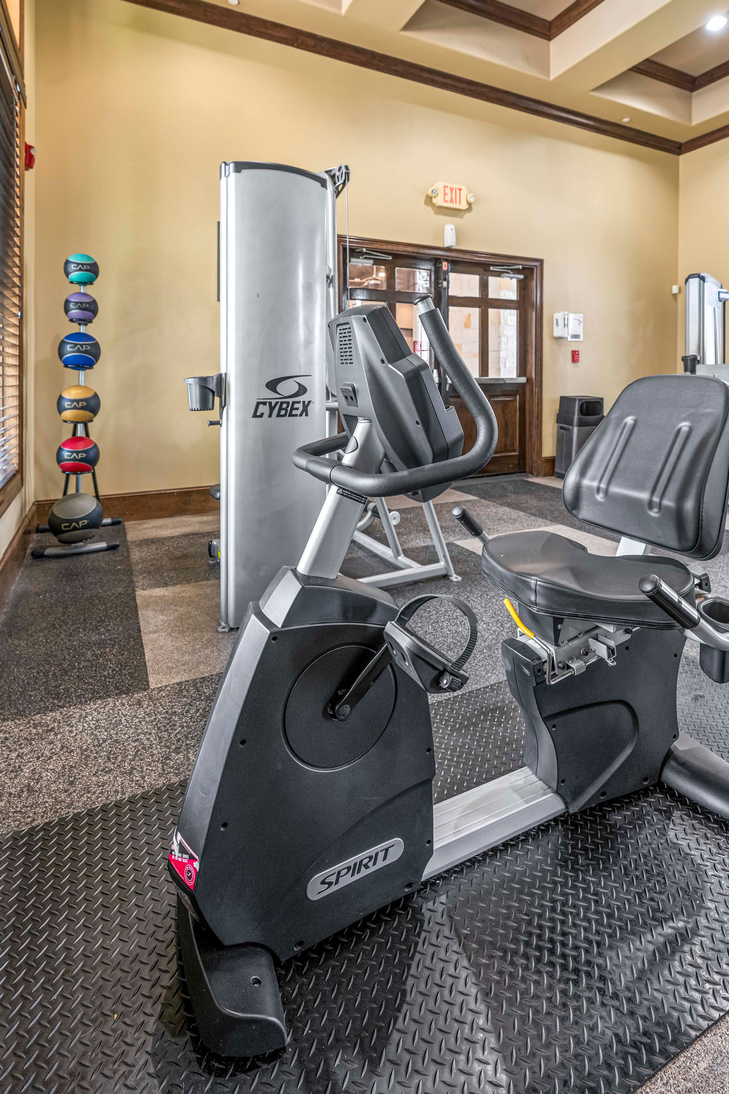 Fitness center with recumbent bike, weight machines, medicine ball rack, rubber flooring, and large windows for natural light