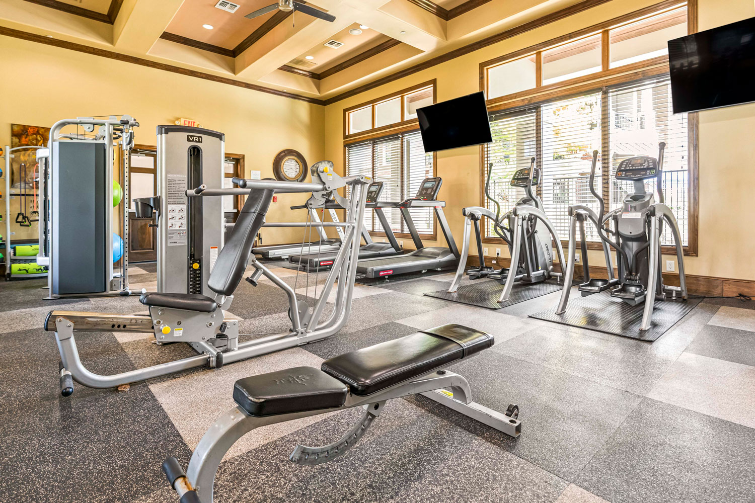 Fitness center with strength machines, treadmills, ellipticals, large windows, wall mounted TVs, and rubber flooring