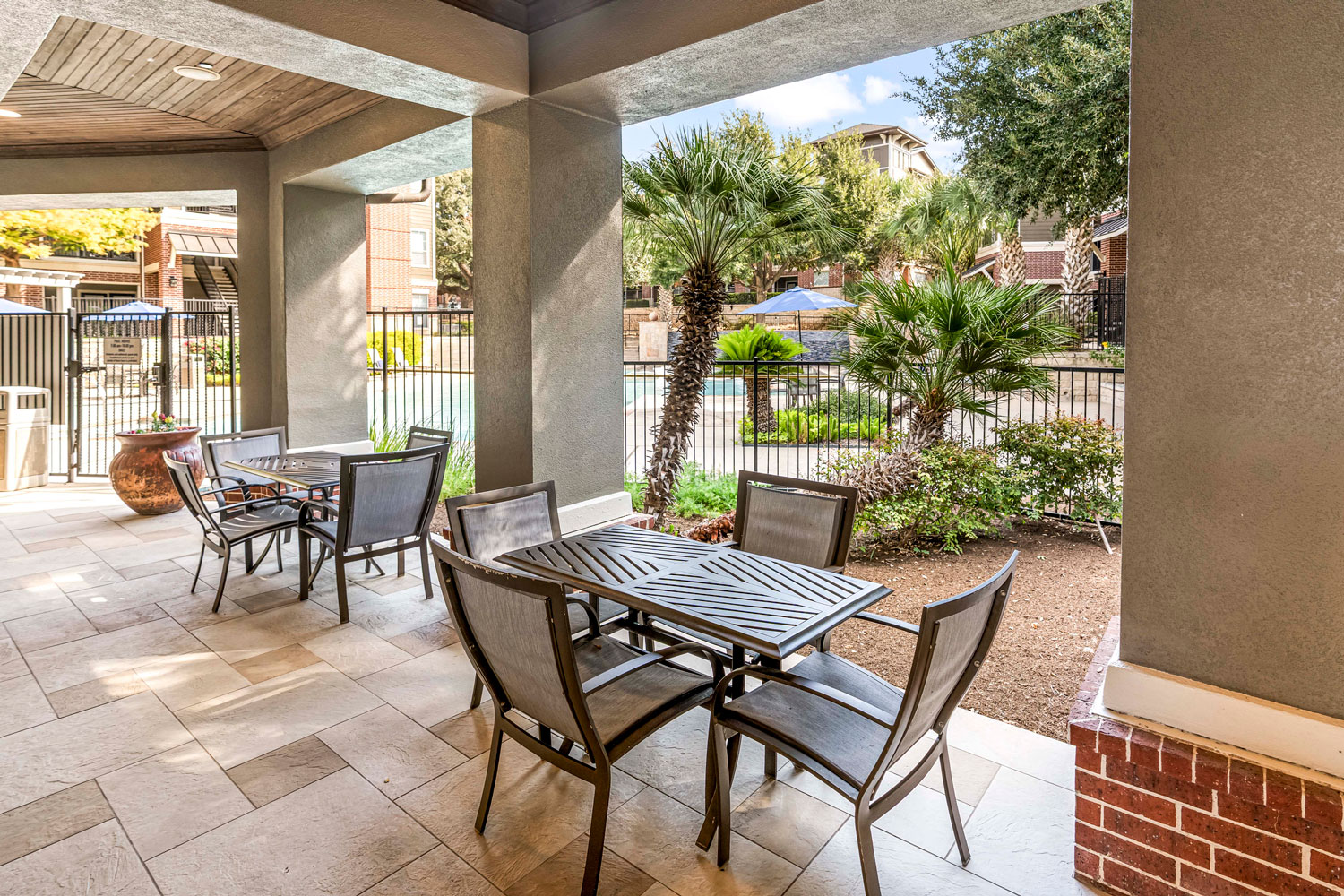 Covered outdoor patio with dining tables and chairs overlooking landscaped courtyard and resort-style swimming pool