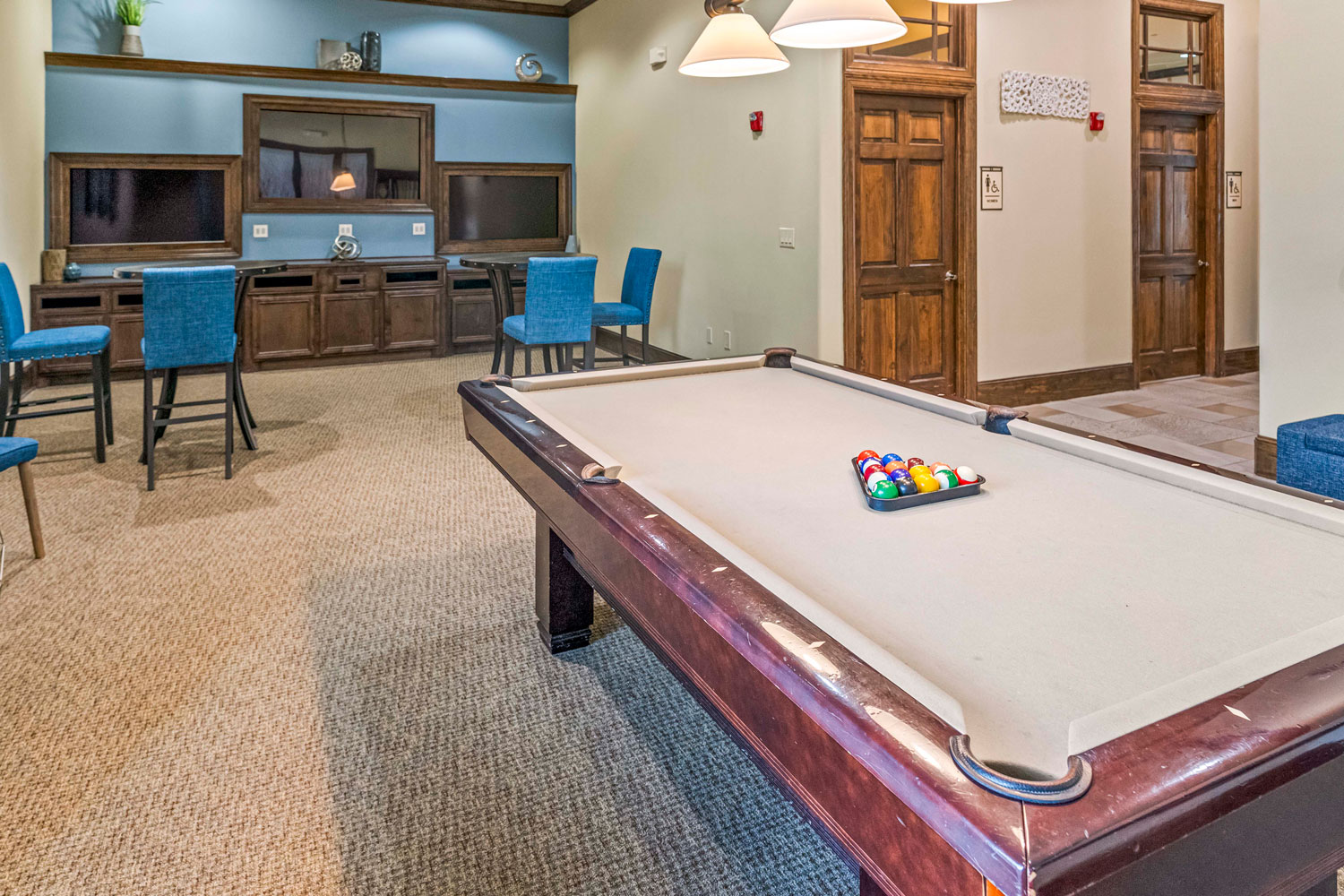 Resident game room with billiards table, bar-height seating area, wood cabinetry media wall, and soft carpet flooring