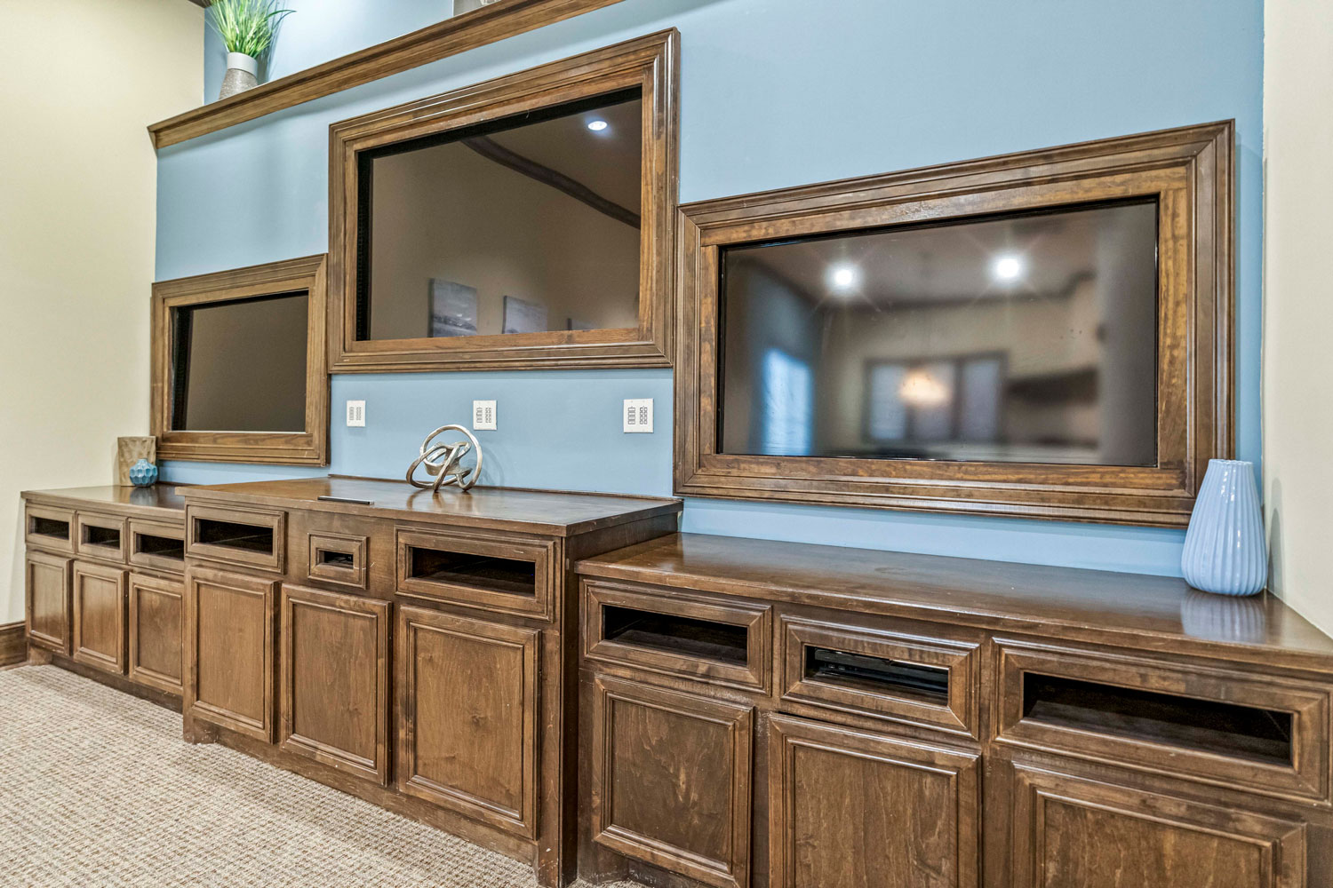 Built-in entertainment wall with framed television spaces, wood cabinetry, display shelves, and decorative accents
