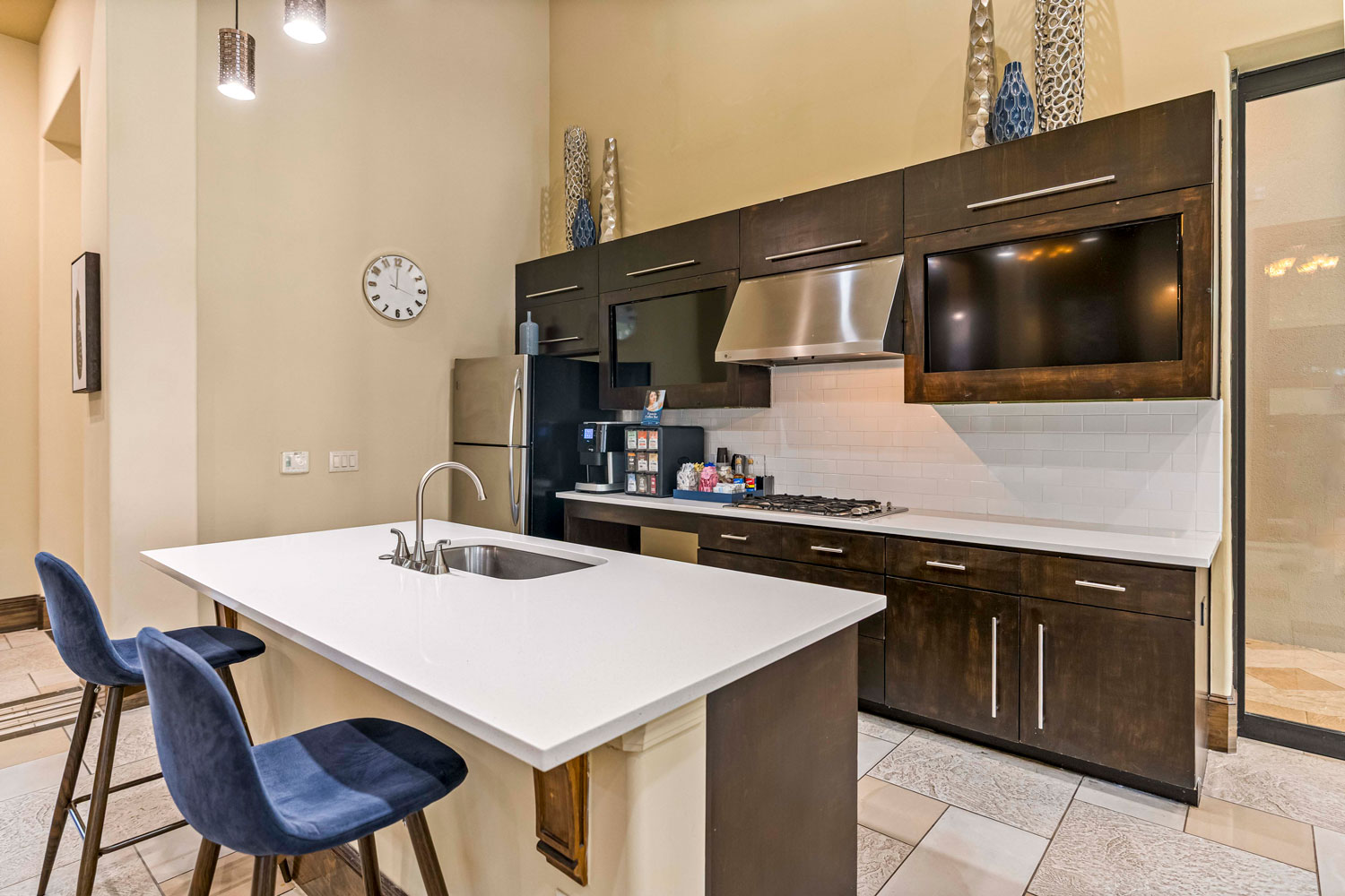 Modern clubhouse kitchen with white island, bar seating, stainless appliances, dark wood cabinets, and decorative lighting