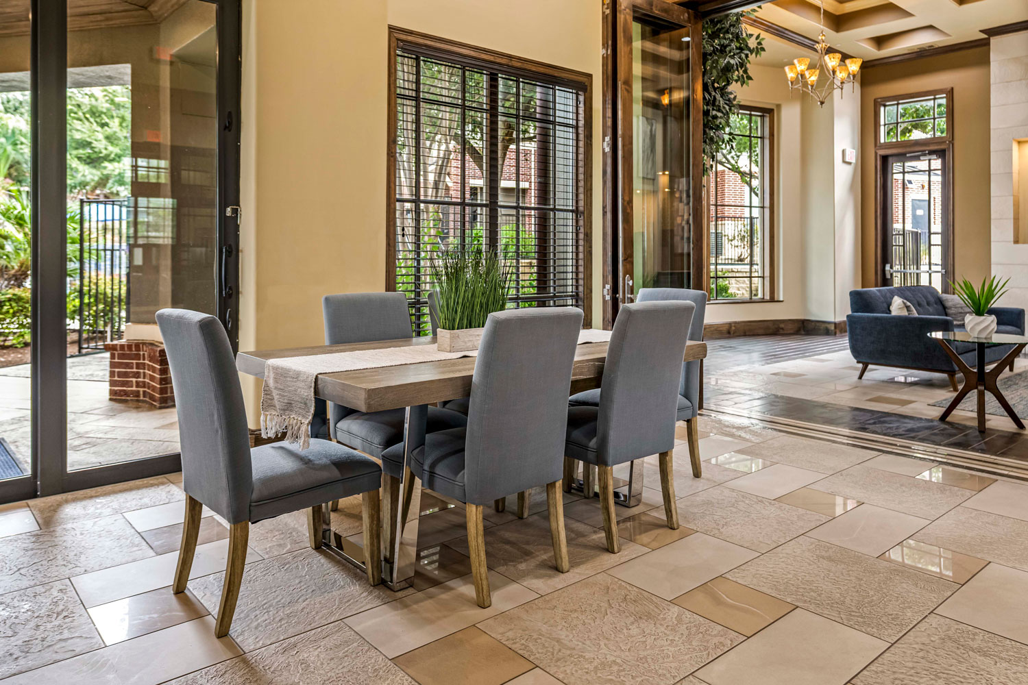 Clubhouse dining area with rectangular table, upholstered chairs, large windows, tile flooring, and lounge seating nearby