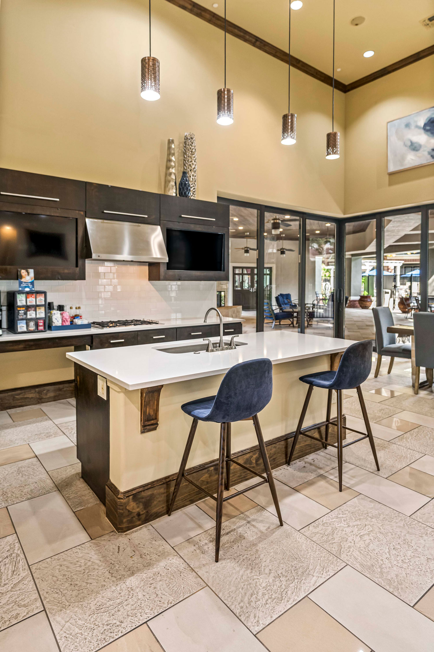 Resident clubhouse kitchen with white island, bar seating, pendant lights, stainless appliances, and dark wood cabinetry