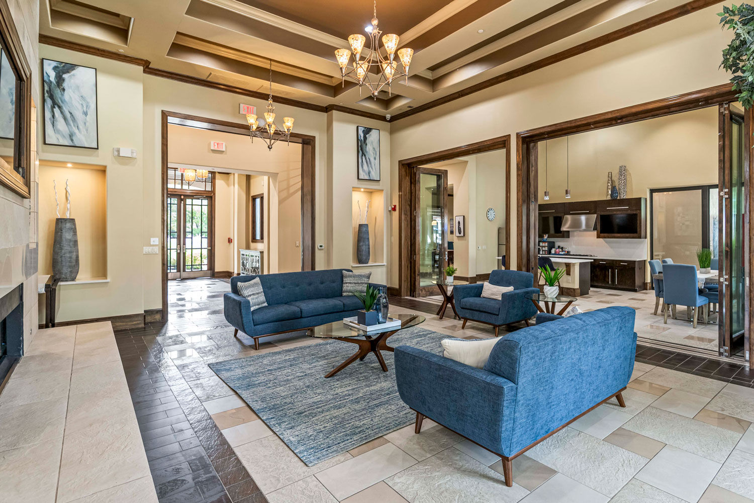 Spacious resident clubhouse lounge with blue sofas, glass tables, coffered ceiling, and open hallway leading to lobby entrance