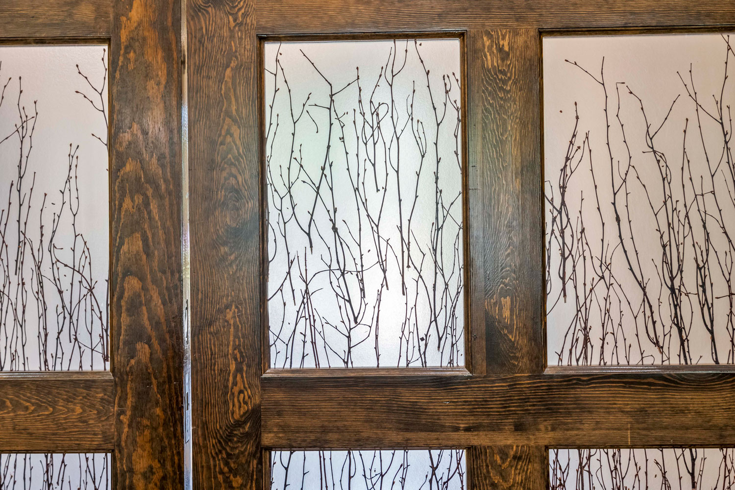 Frosted glass sliding doors with decorative branch pattern set in dark wood frames at apartment clubhouse entrance