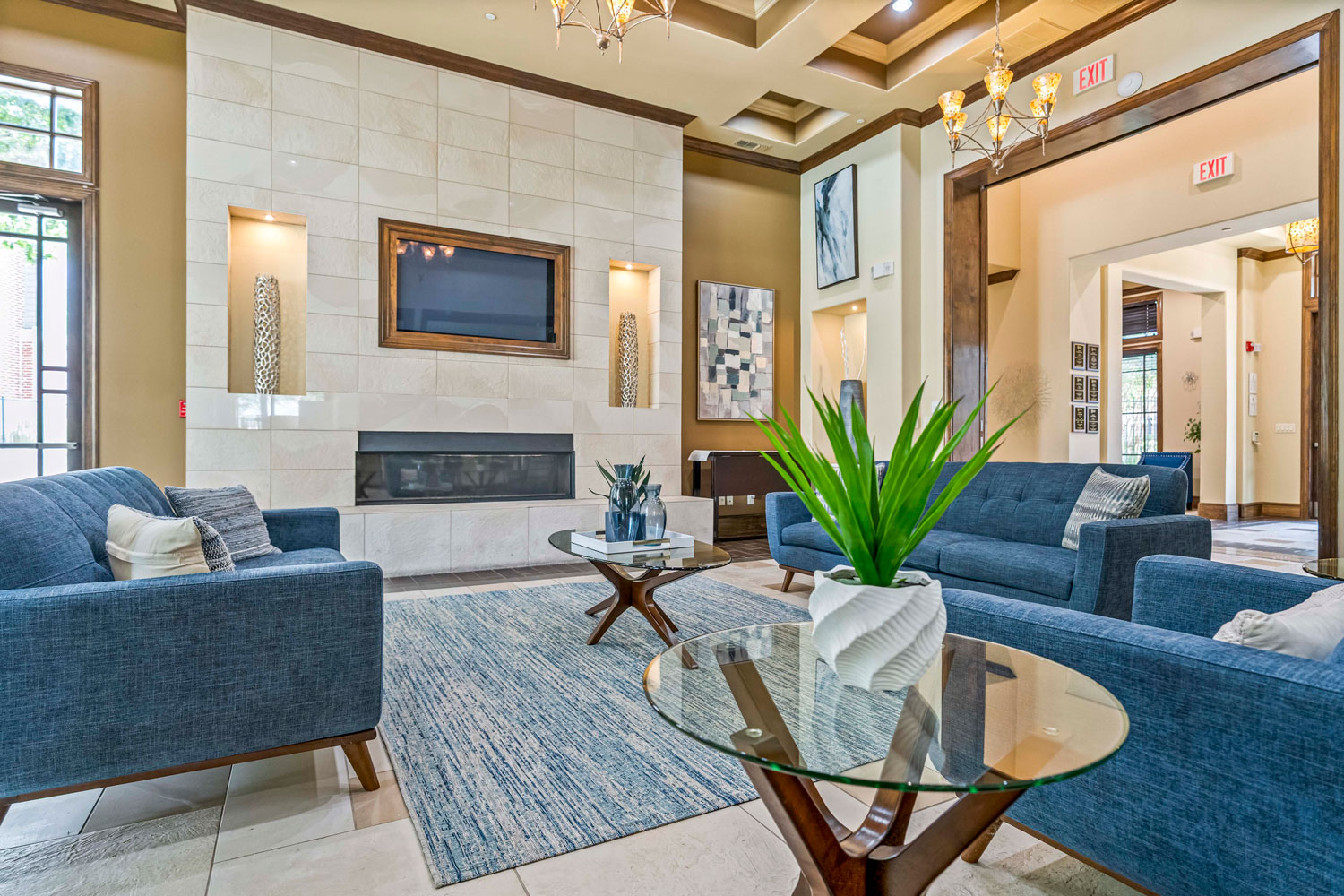 Clubhouse lounge with blue sofa, glass coffee table, tall windows overlooking courtyard, tile flooring, and decorative chandelier lighting