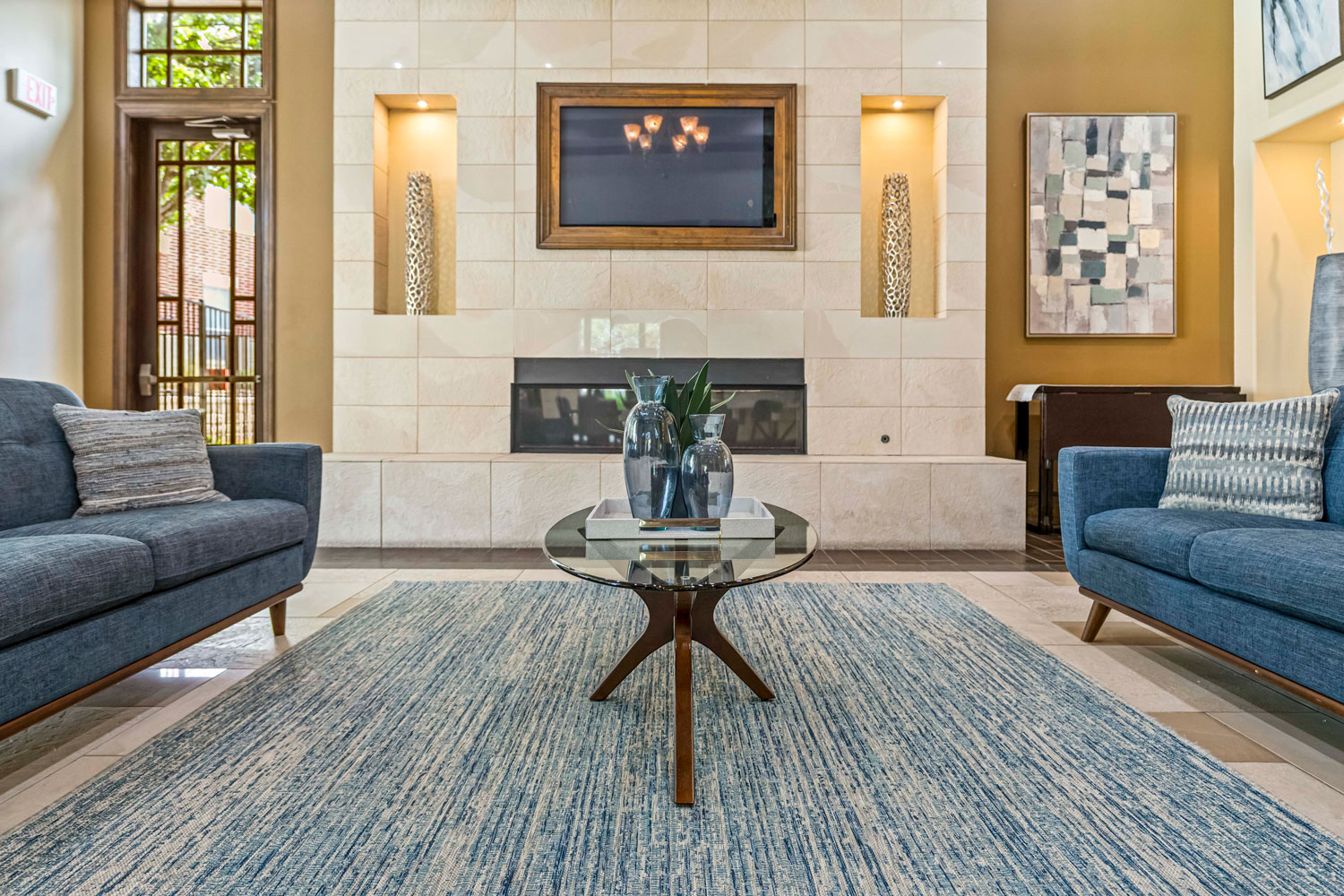 Resident clubhouse lounge with fireplace feature wall, built in display niches, blue sofas, and round glass coffee table