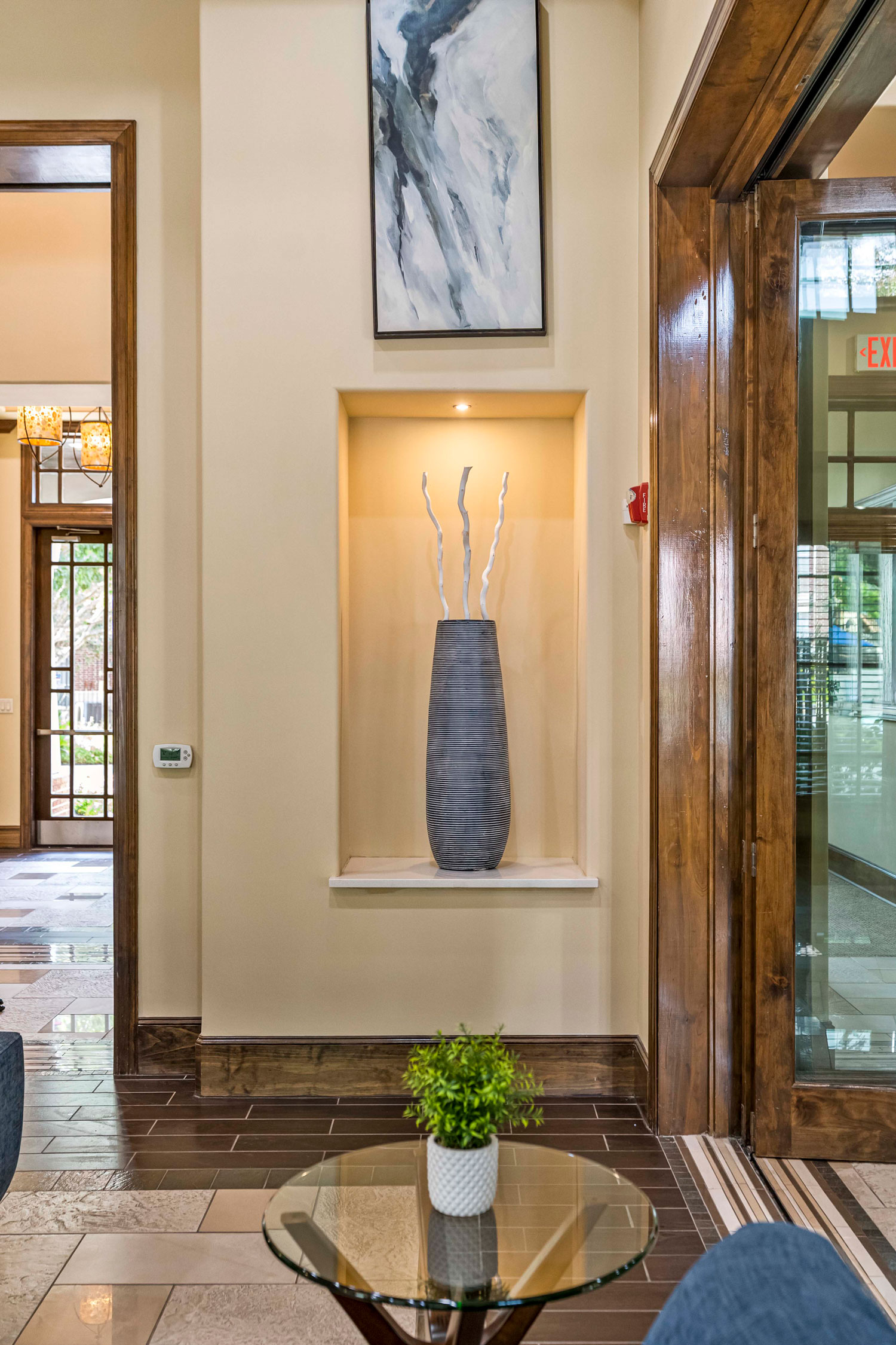 Clubhouse lobby niche with tall decorative vase, wood trim accents, tile flooring, and glass coffee table with plant