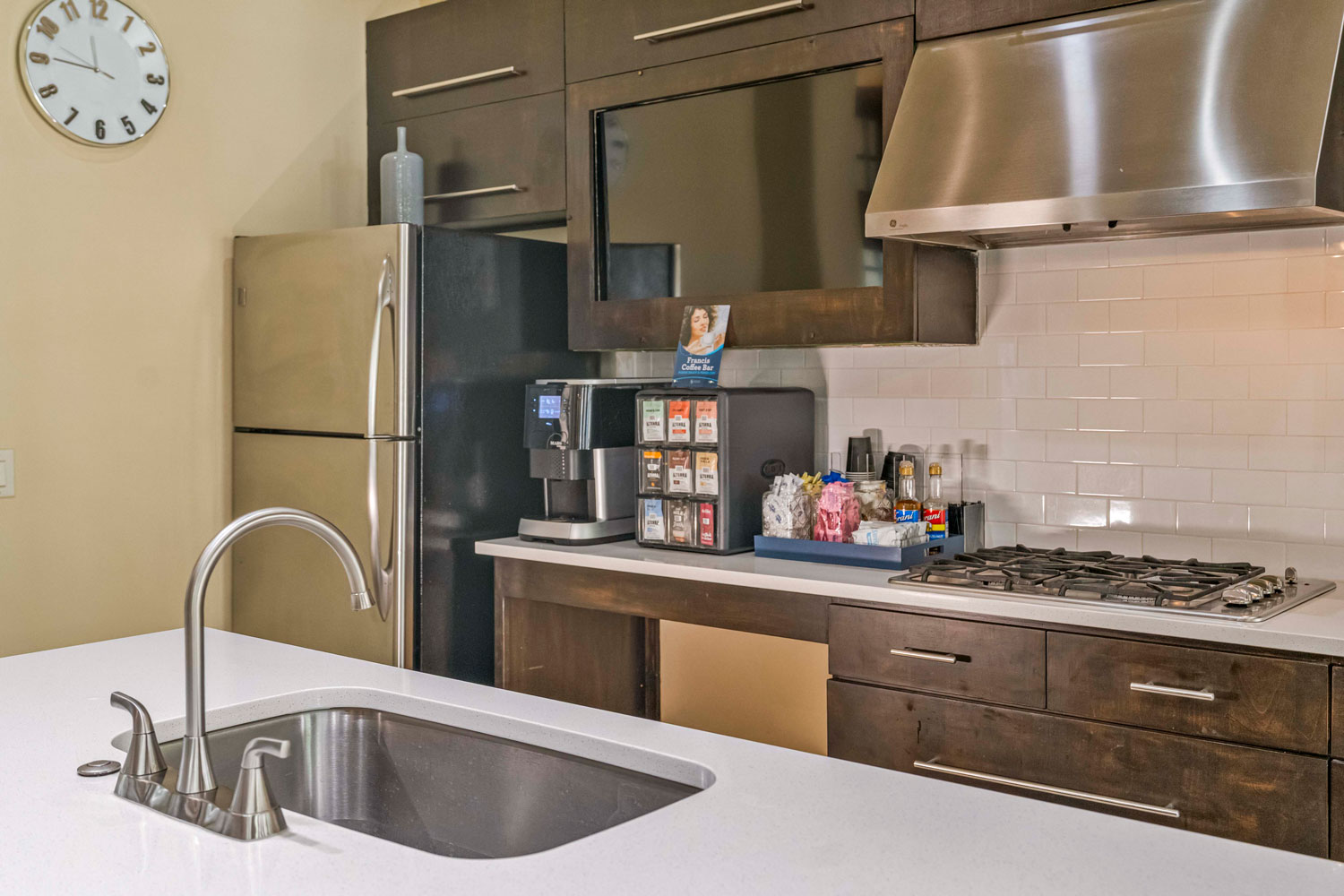 Resident clubhouse kitchen with stainless appliances, gas cooktop, coffee station, subway tile backsplash, and quartz countertop island