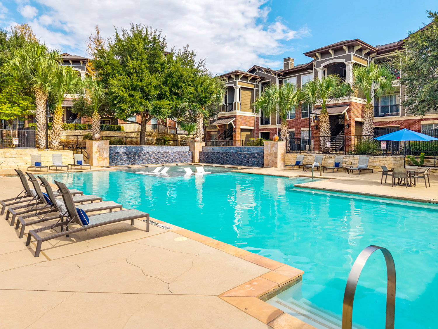 Resort style swimming pool and clubhouse at sunset with lounge chairs, umbrellas, patio seating, and landscaped courtyard