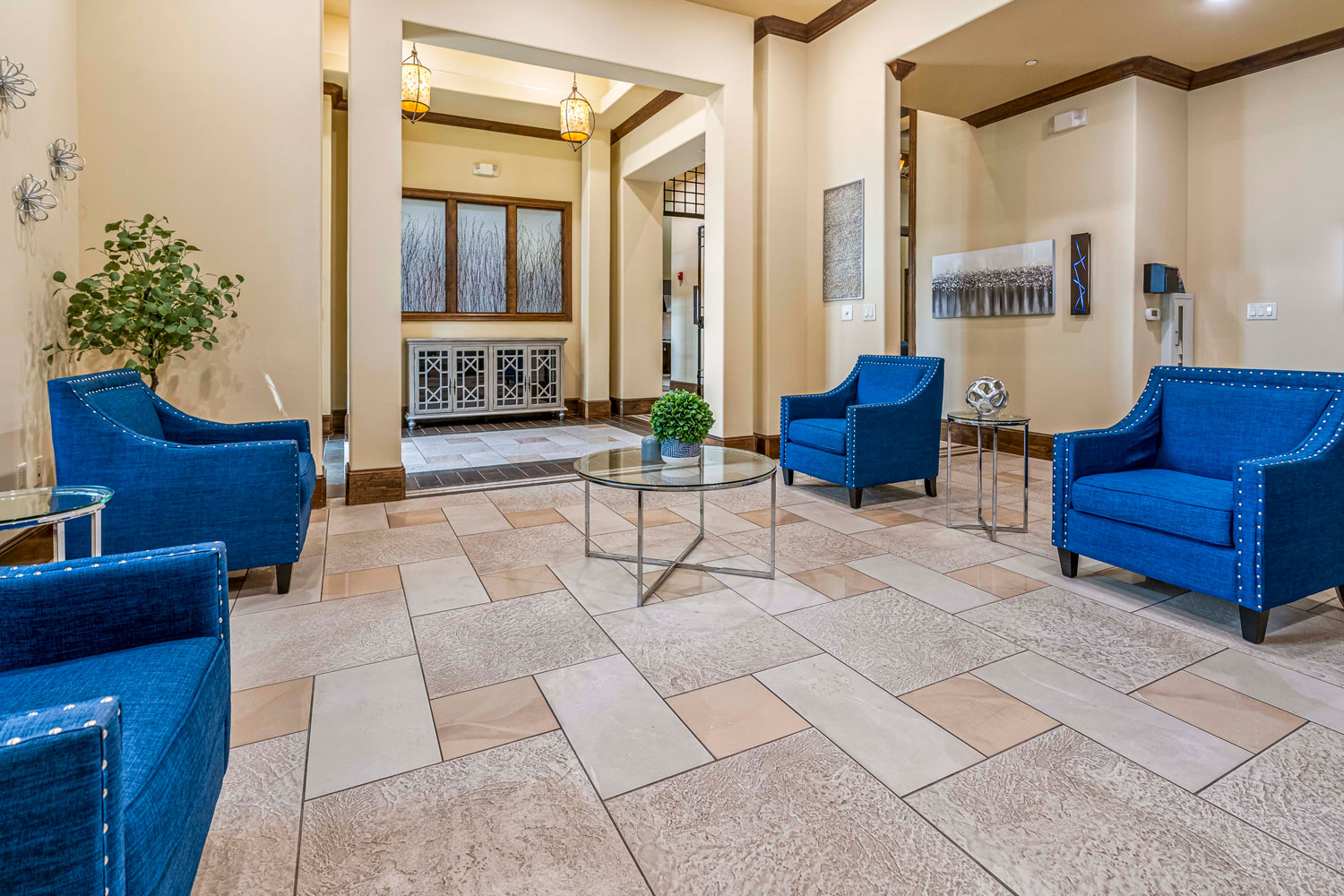 Clubhouse lobby lounge with blue upholstered chairs, glass coffee table, tiled flooring, and decorative wall art
