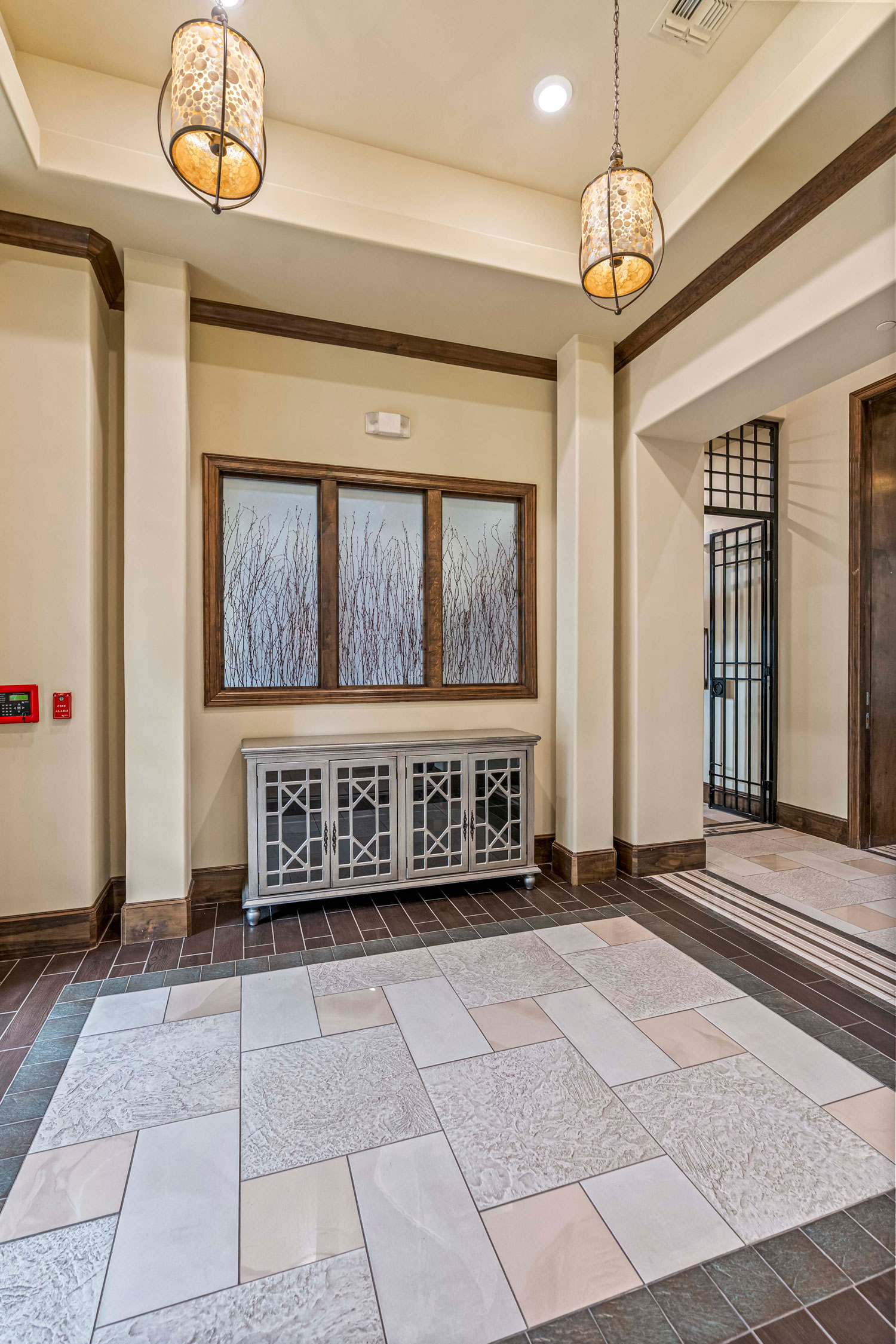 Apartment clubhouse entry hall with pendant lighting, decorative cabinet, tiled flooring, and framed wall art
