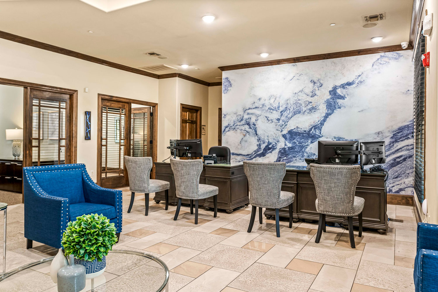 Leasing office area with marble accent wall, service desk with computers, upholstered guest chairs, and tiled clubhouse flooring