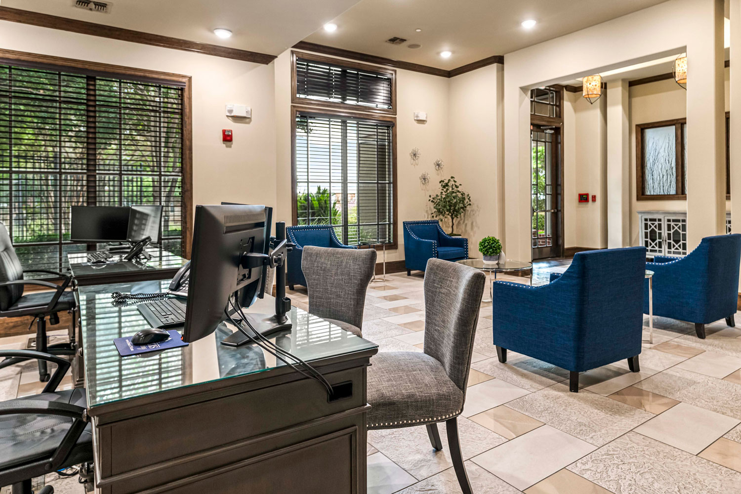 Business center workspace with desktop computers, glass desk surfaces, upholstered chairs, and lounge seating near large windows