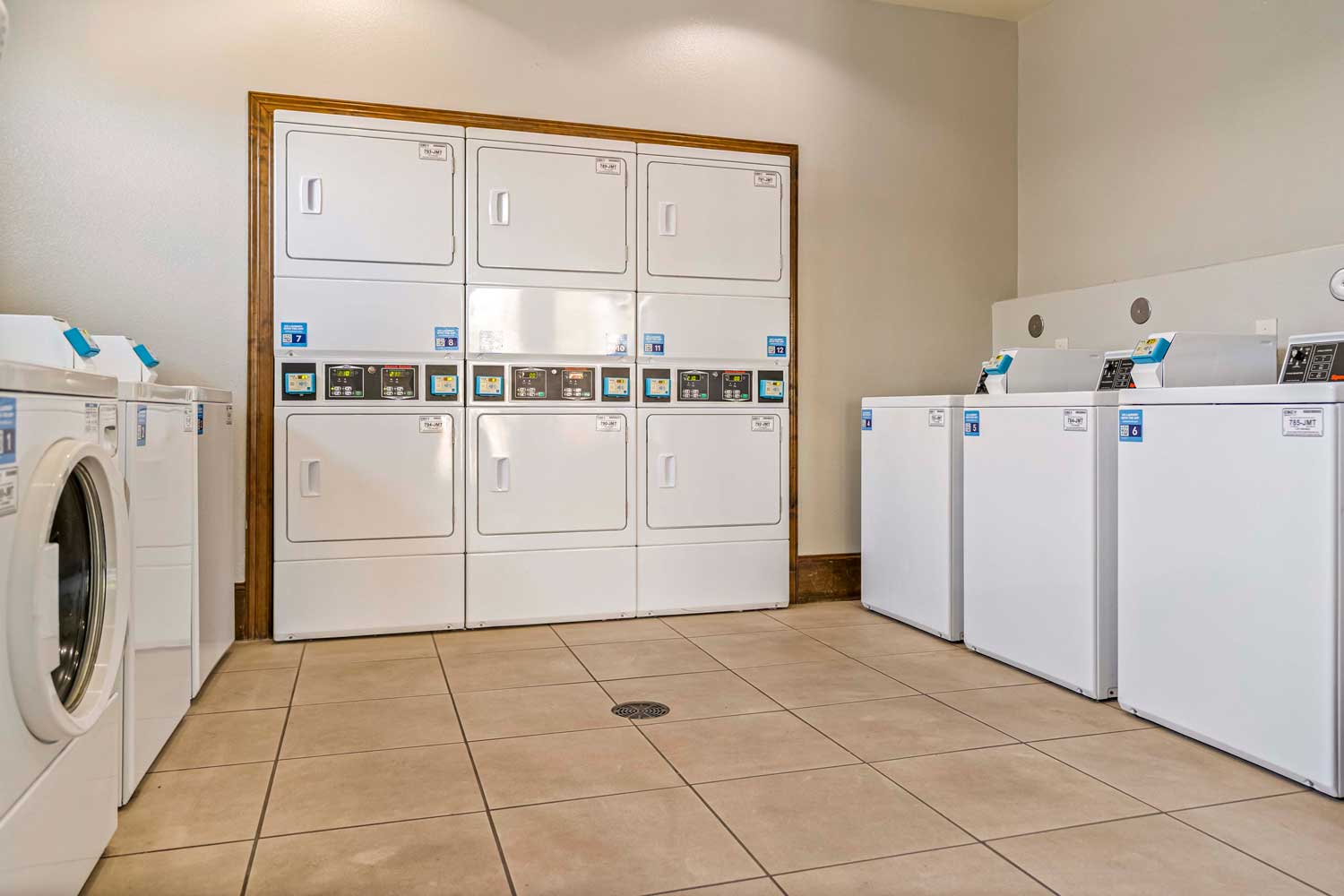 Clean community laundry room with stacked dryers, front-load washers, tile flooring, and bright lighting for resident convenience