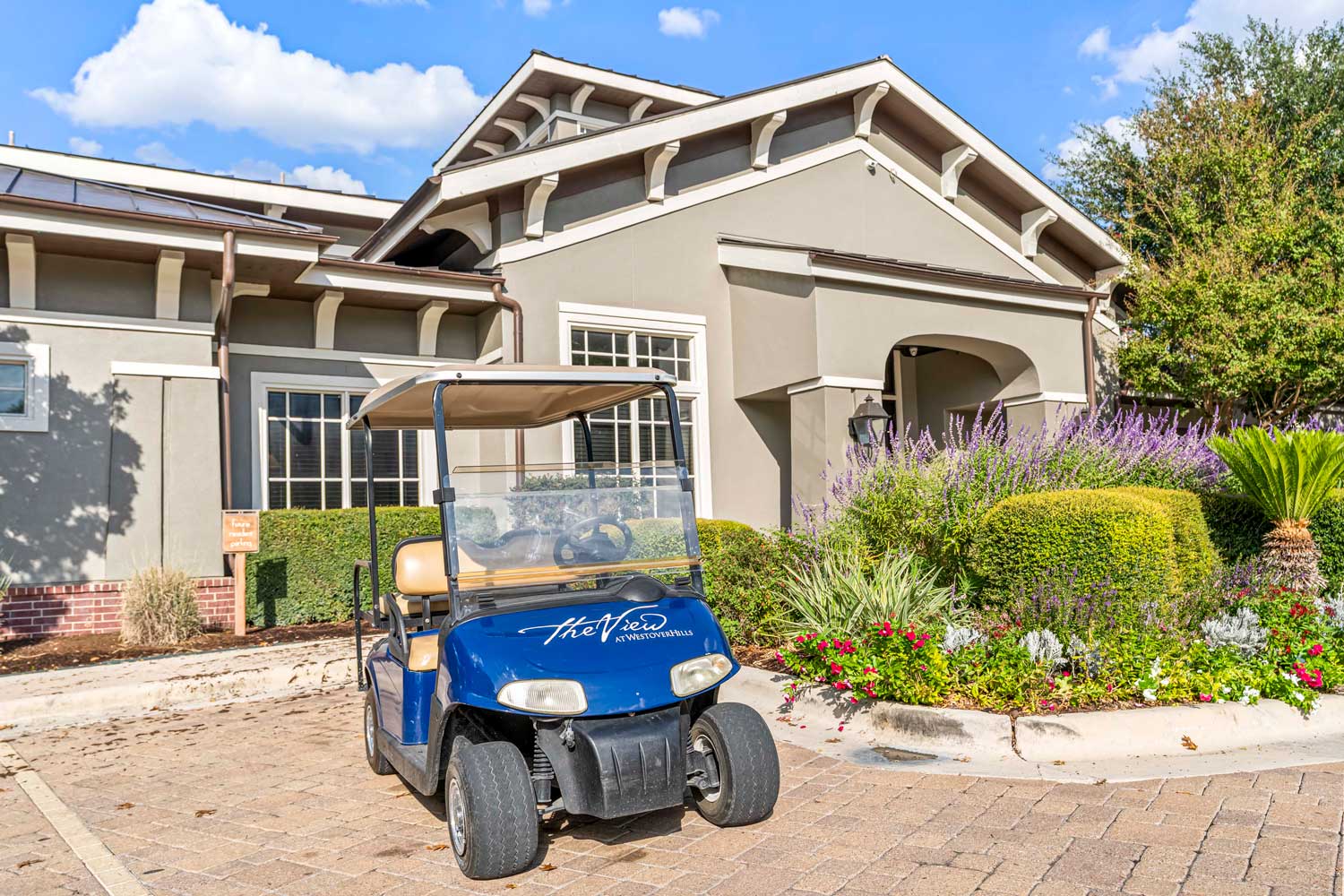 A branded blue golf cart parked in front of The View at Westover Hills leasing office with colorful landscaping