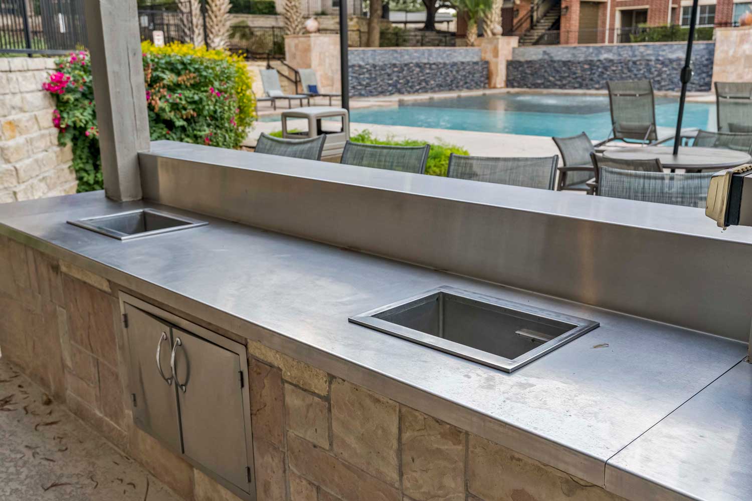 Outdoor grilling station with stainless countertop, prep sinks, and poolside patio seating overlooking resort style pool