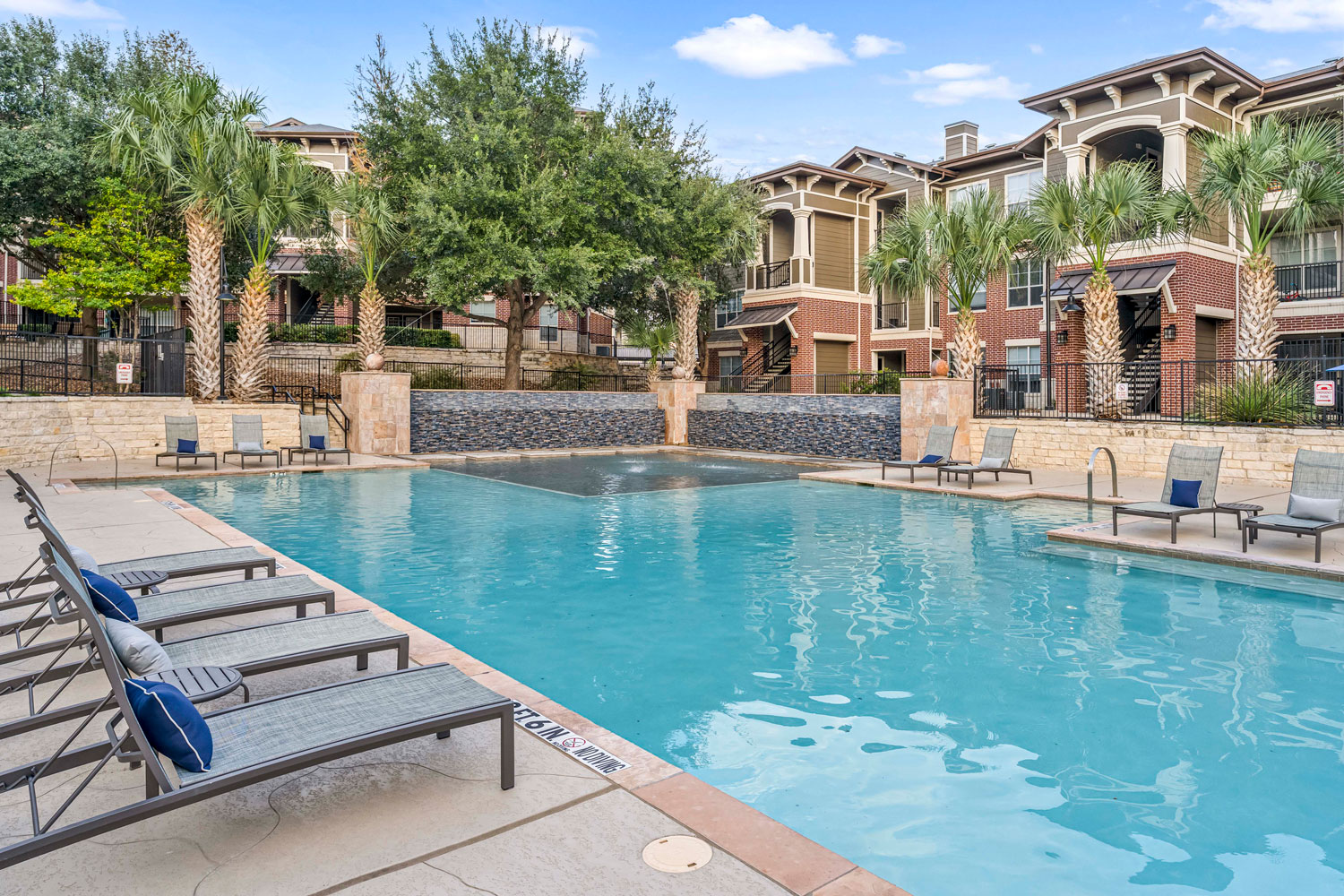 Covered poolside pavilion with grilling station, prep sink, round dining tables, and lounge chairs beside swimming pool