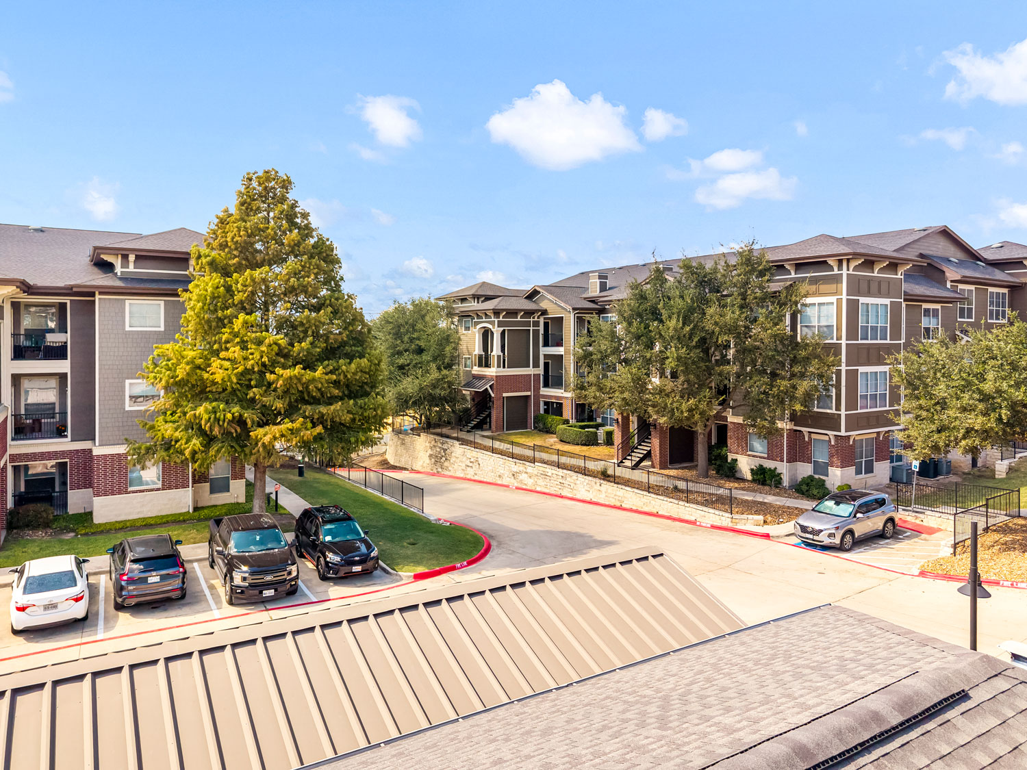 Aerial view of a multi-building brick apartment community featuring a central parking lot, mature trees, and landscaped grounds