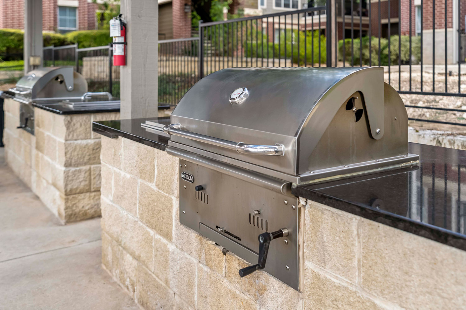 Close view of stainless steel built-in grill with thermometer lid, stone base counter, and outdoor cooking station in resident pavilion