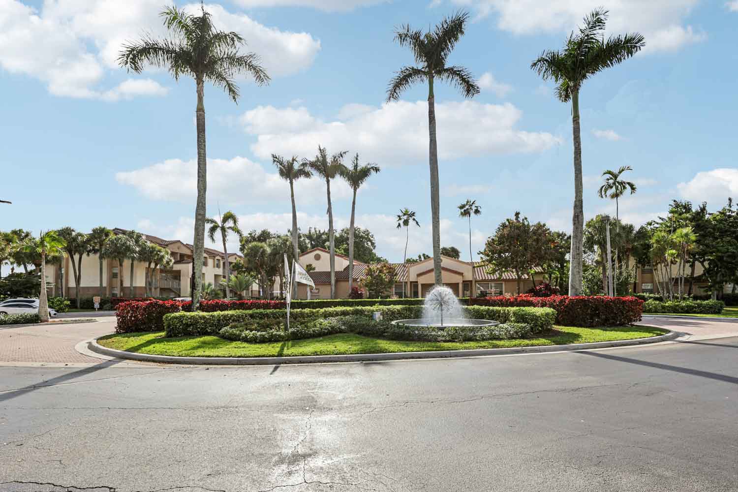 Palm lined community entrance with fountain and manicured hedges under blue sky