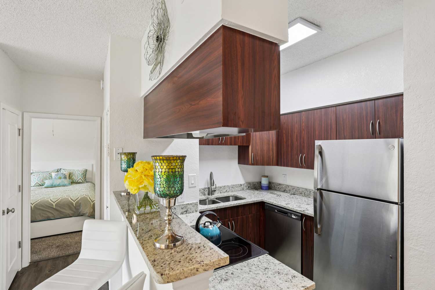 Kitchen with granite breakfast bar, stainless steel appliances, dark wood cabinets, and open view to bedroom