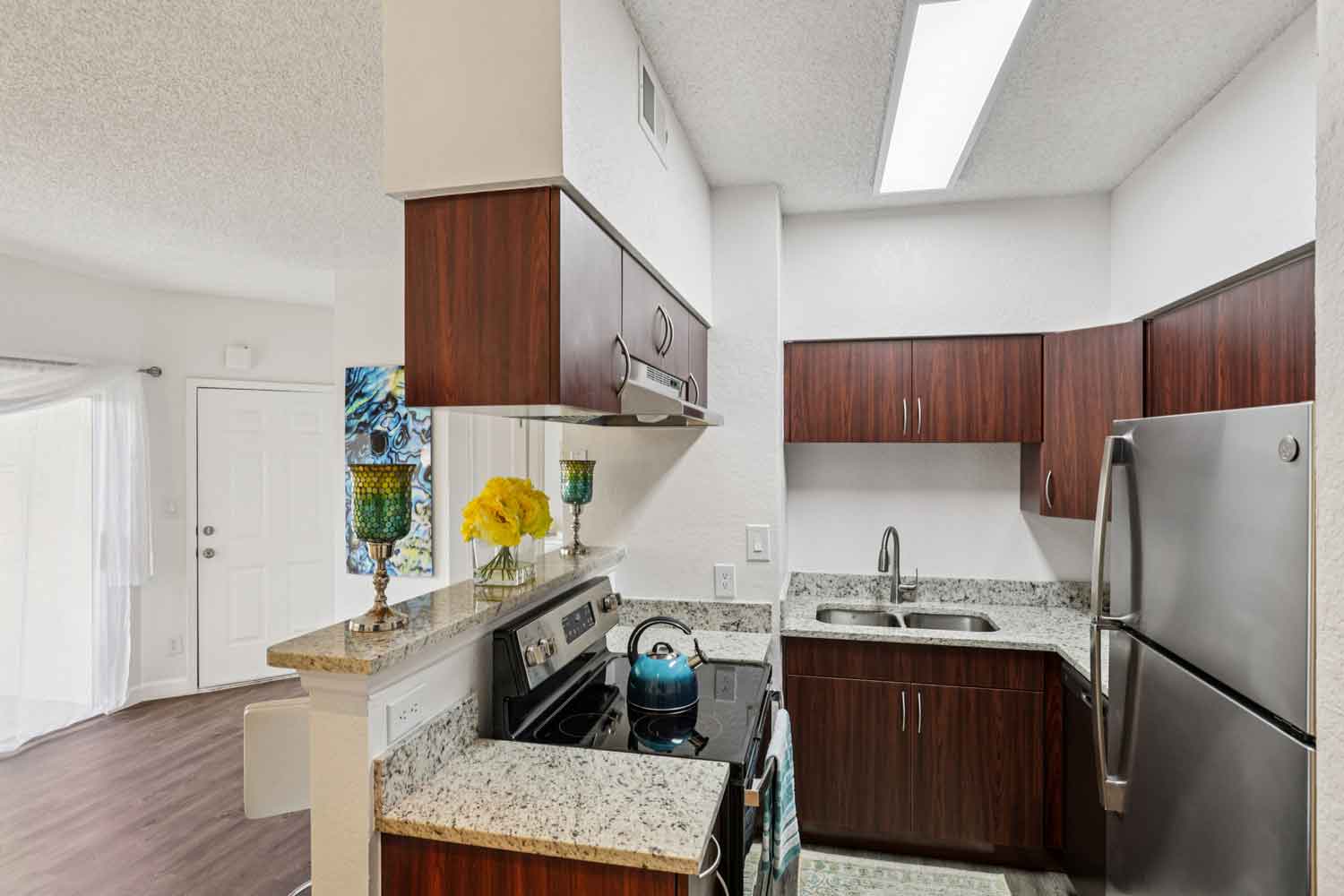 Compact kitchen with electric range, double sink, granite counters, dark cabinetry, and overhead lighting