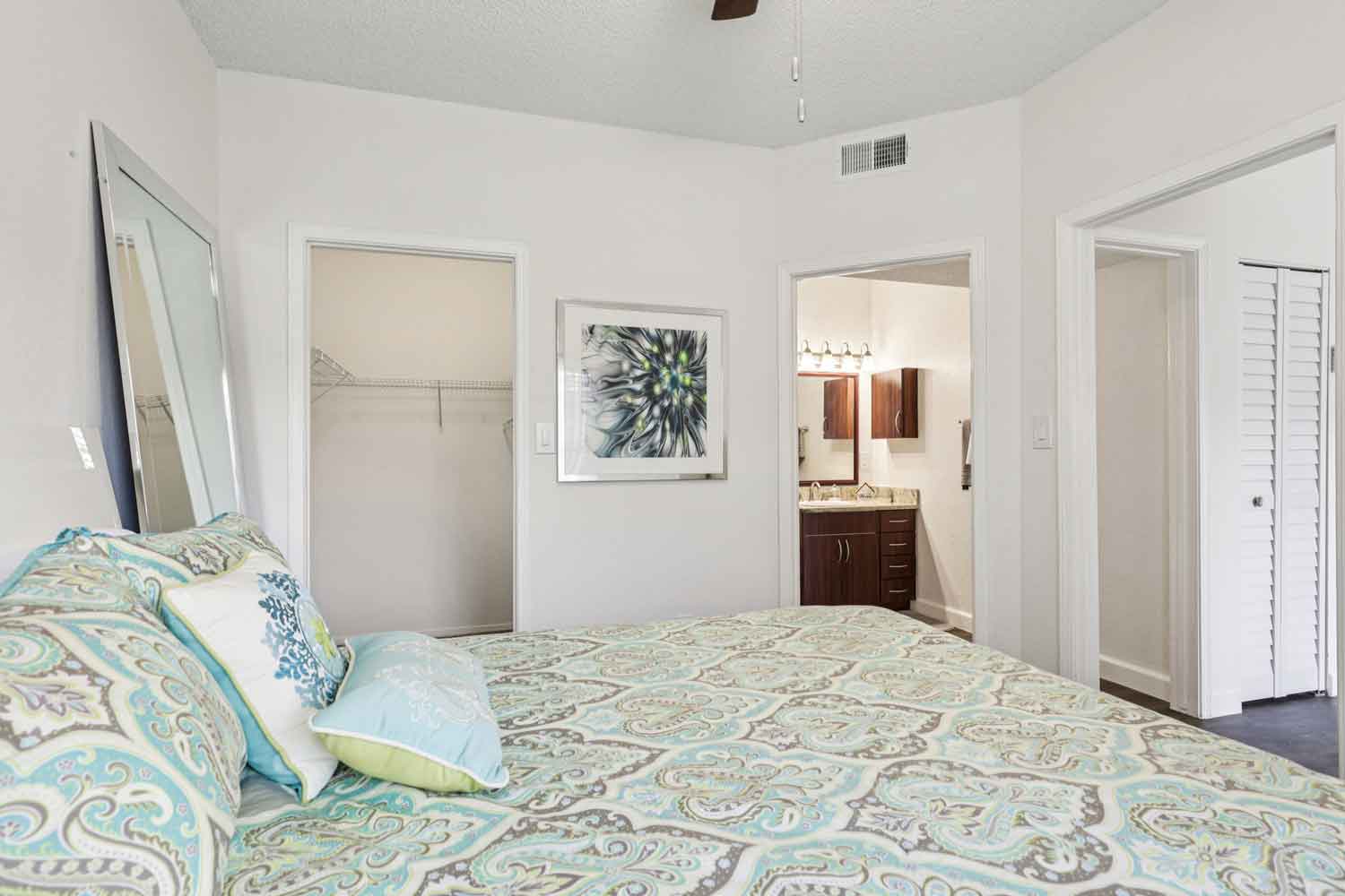Bedroom with patterned bedding, large wall mirror, open closet, and view into attached bathroom