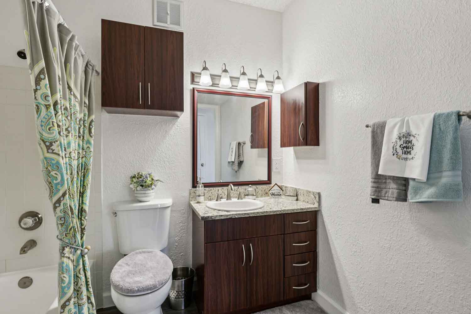Bathroom with granite countertop vanity, wood cabinets, framed mirror, modern lighting, and tub shower combo