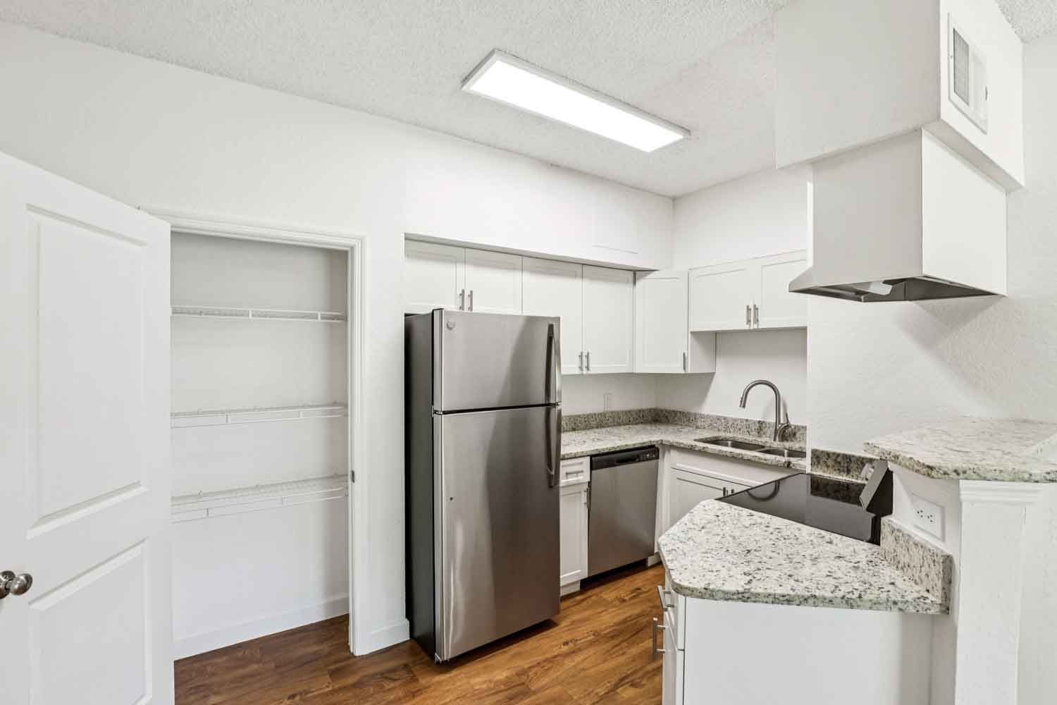 Kitchen with granite counters, stainless steel appliances, white cabinetry, and open pantry shelving beside refrigerator