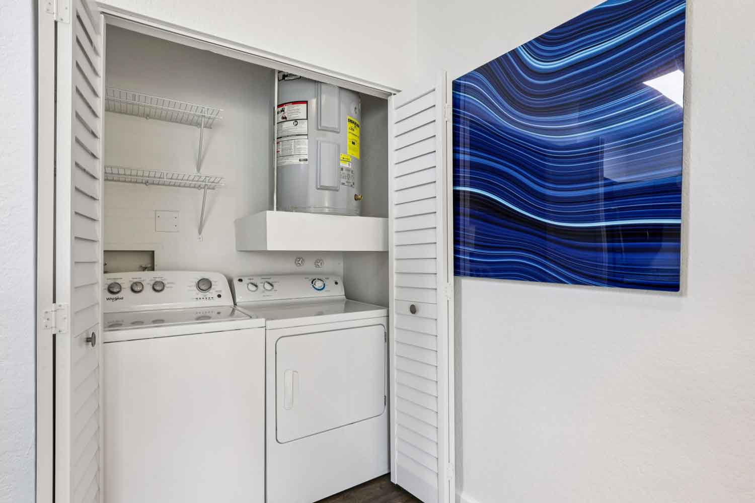 In-unit laundry closet with full-size washer and dryer, wire shelving, water heater, and white louvered doors