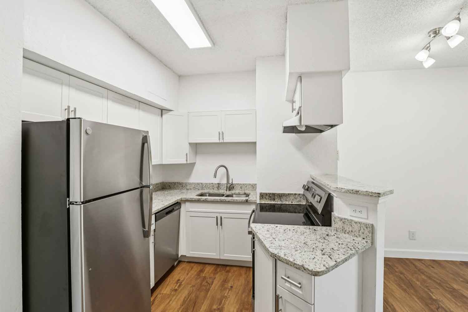 Compact kitchen with stainless steel refrigerator, granite countertops, white cabinets, and wood style flooring