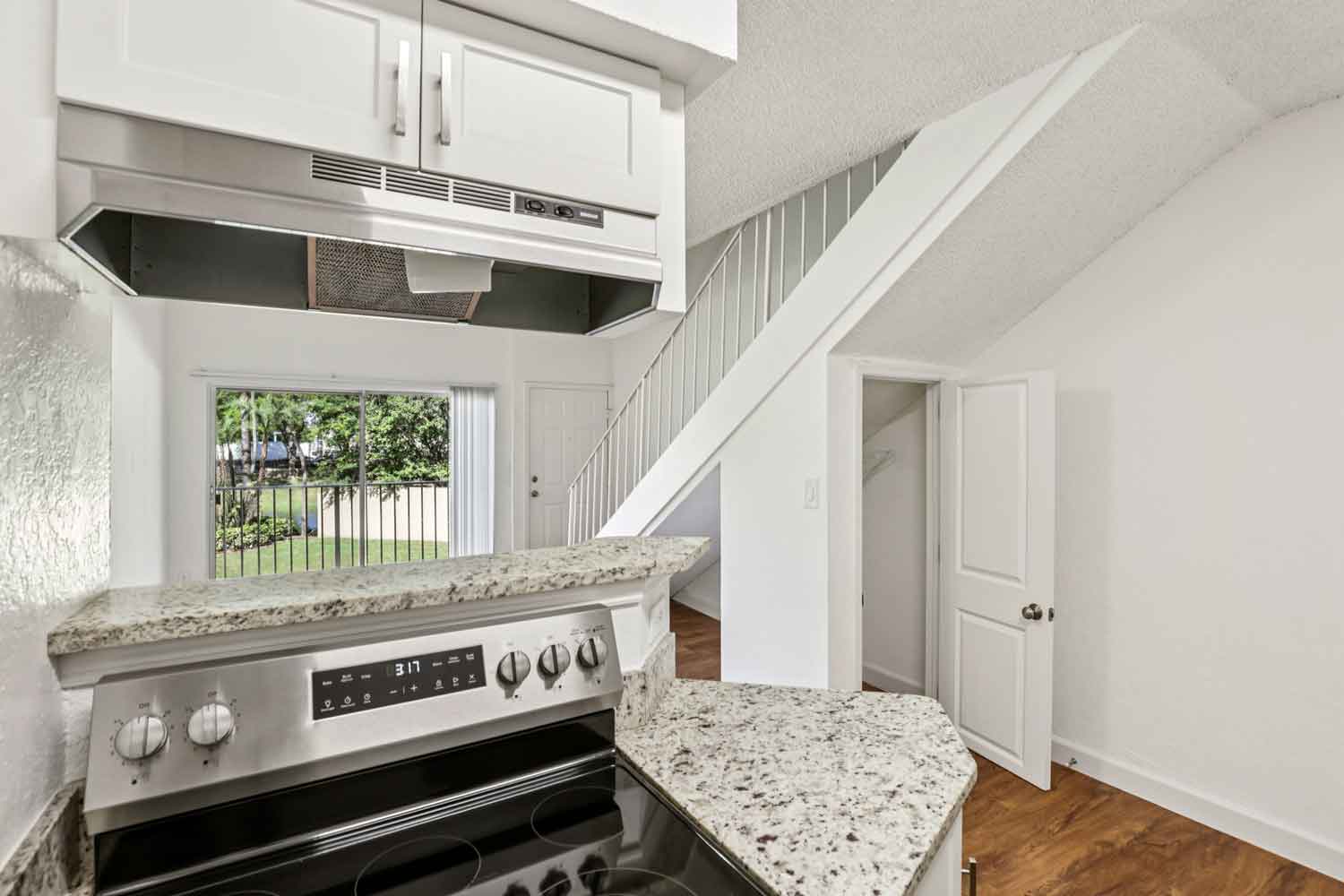 Kitchen view with granite breakfast bar, stainless steel range, white cabinetry, and staircase beside living area