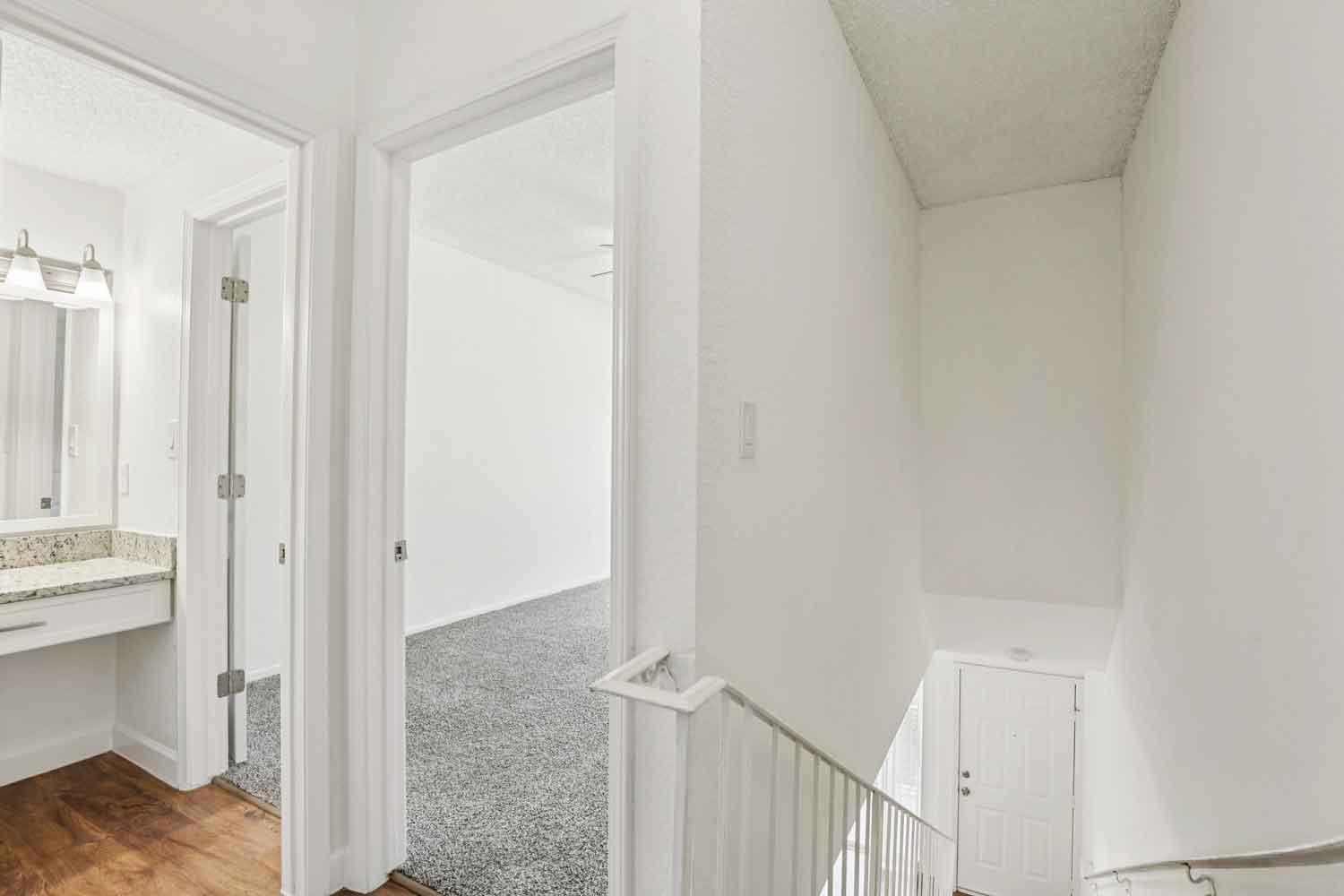 Upstairs hallway with wood style flooring, granite vanity area, bedroom entry, and staircase leading to front door