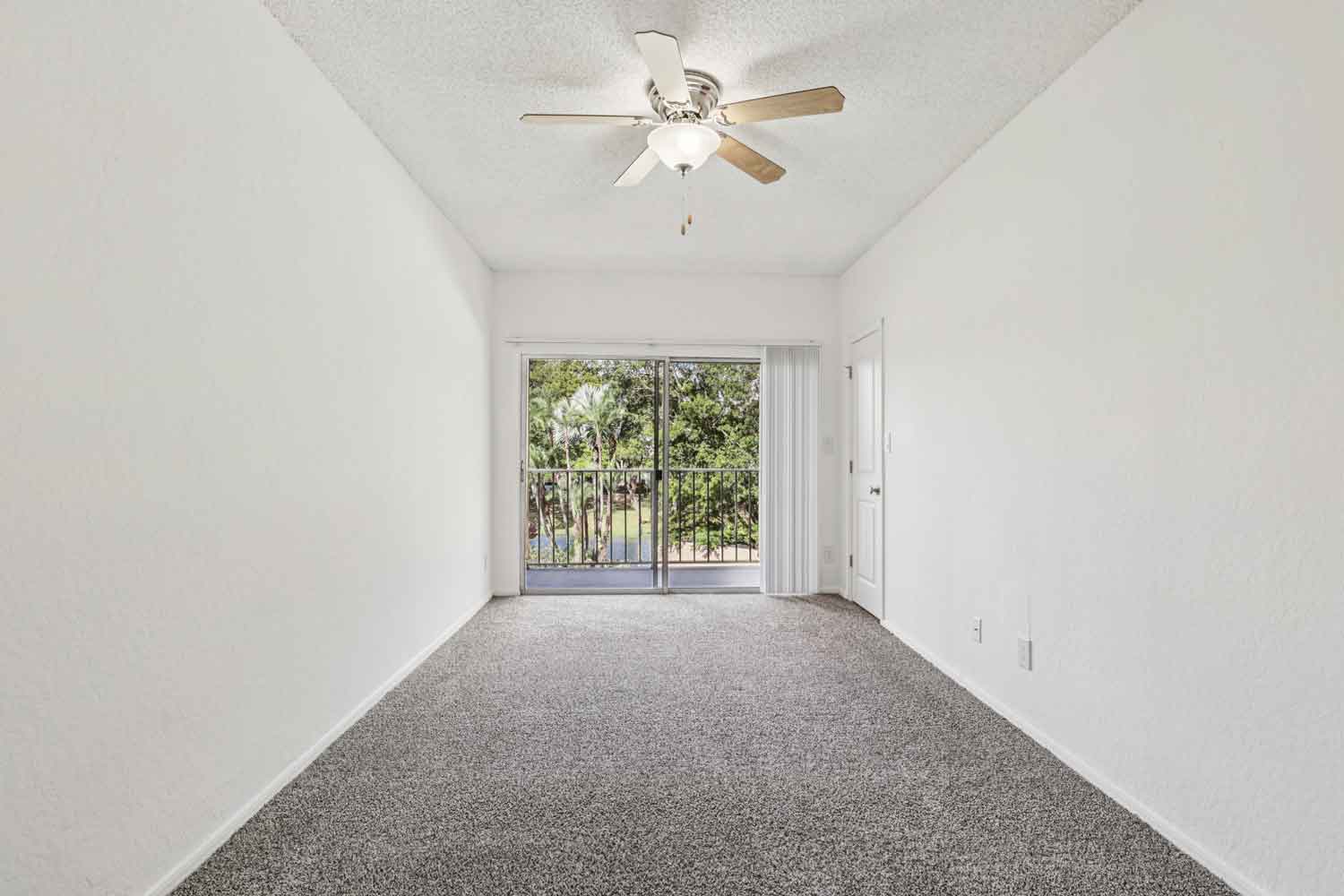 Bedroom with plush carpet, ceiling fan, and sliding glass doors opening to private balcony with trees